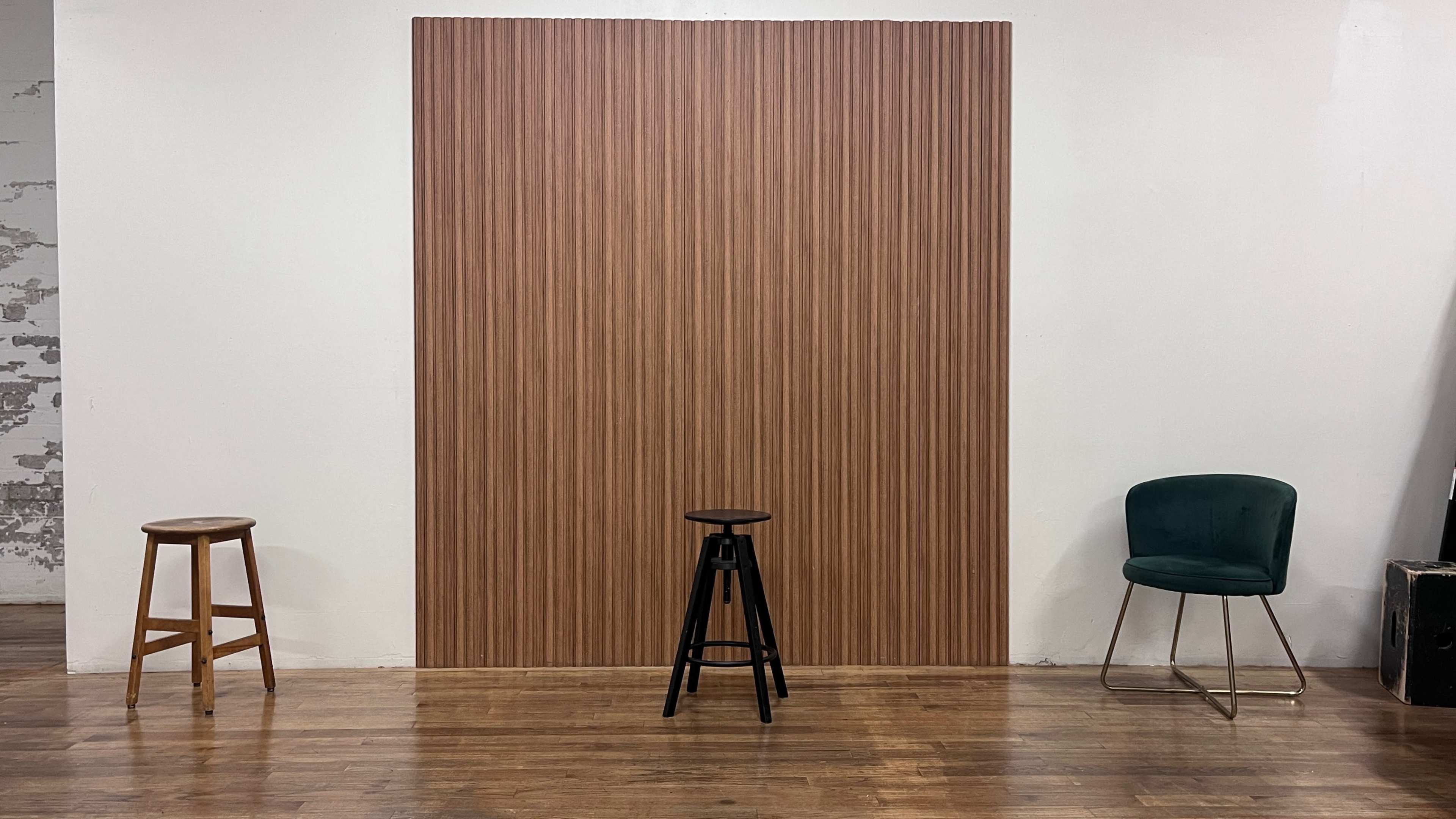 The image shows three stools arranged in front of a vertical striped wood panel on a hardwood floor.