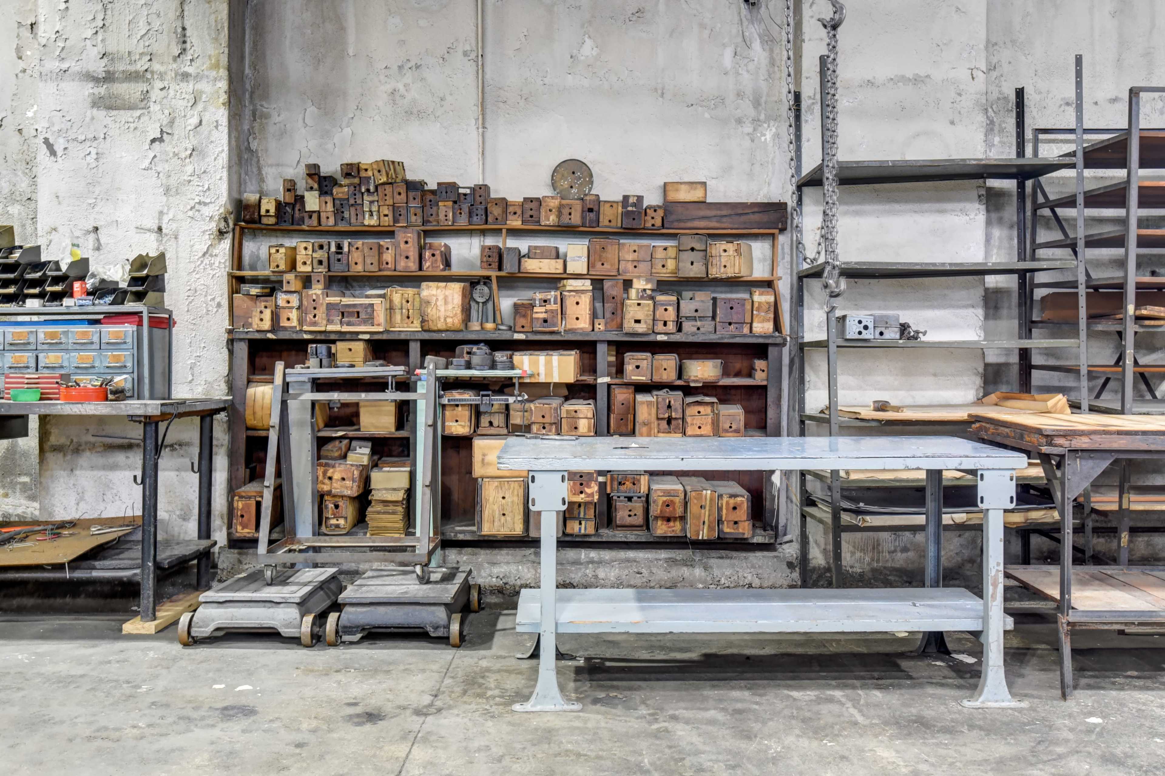 The image shows a workshop with wooden storage boxes stacked on shelves, metal tables, and tools organized on a wall.
