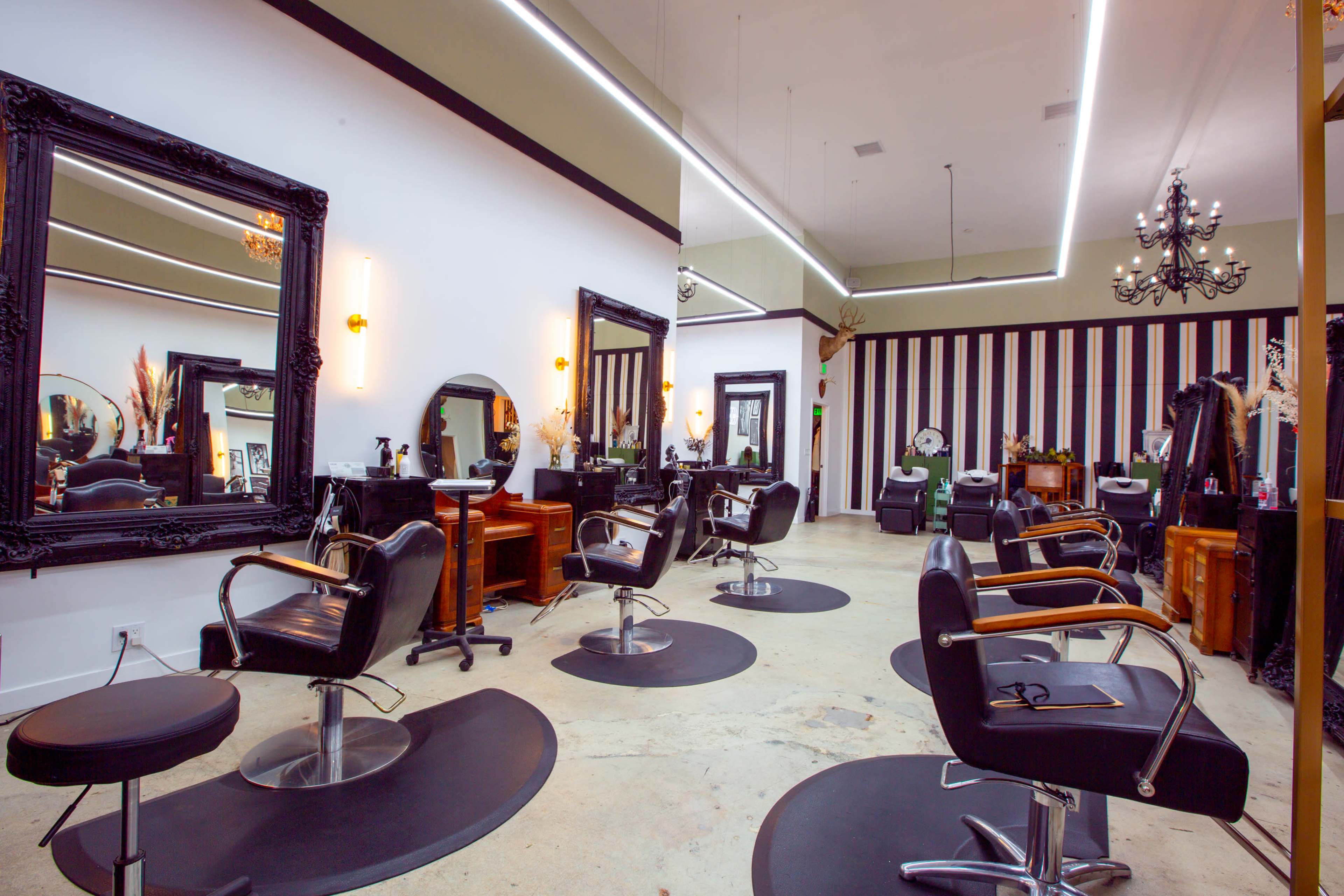 A modern hair salon with black styling chairs, large mirrors, and striped walls.