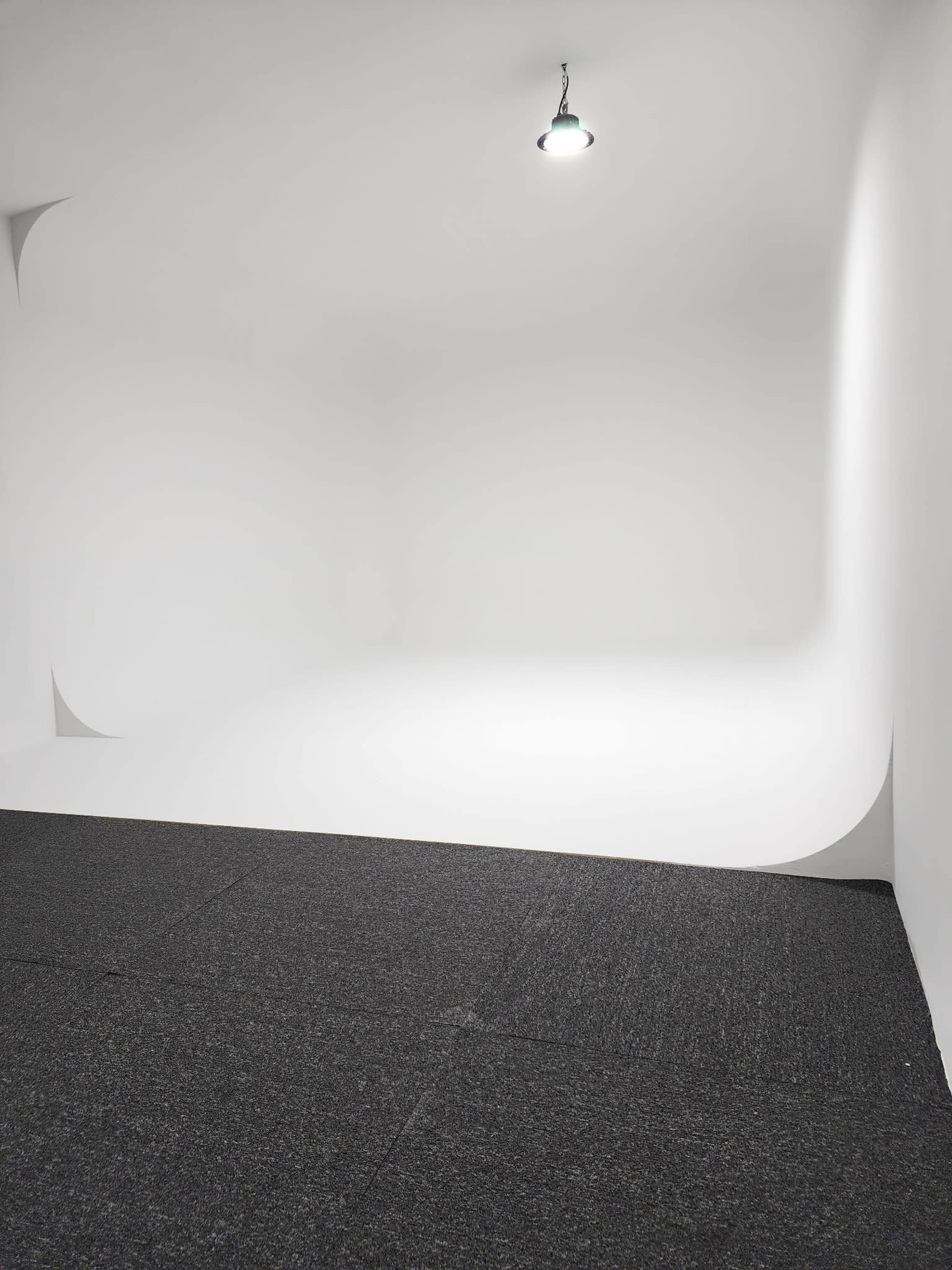 The image shows a minimalist studio space with a white curved backdrop and a dark gray floor.