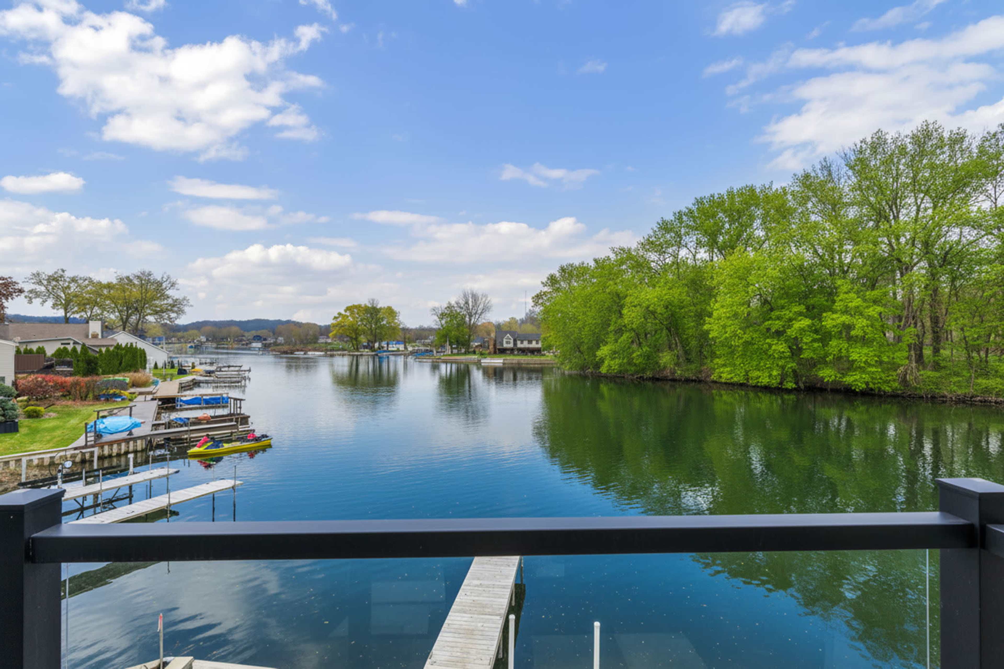 The image shows a calm lake surrounded by trees and residential buildings, with docks and boats visible along the waterfront.