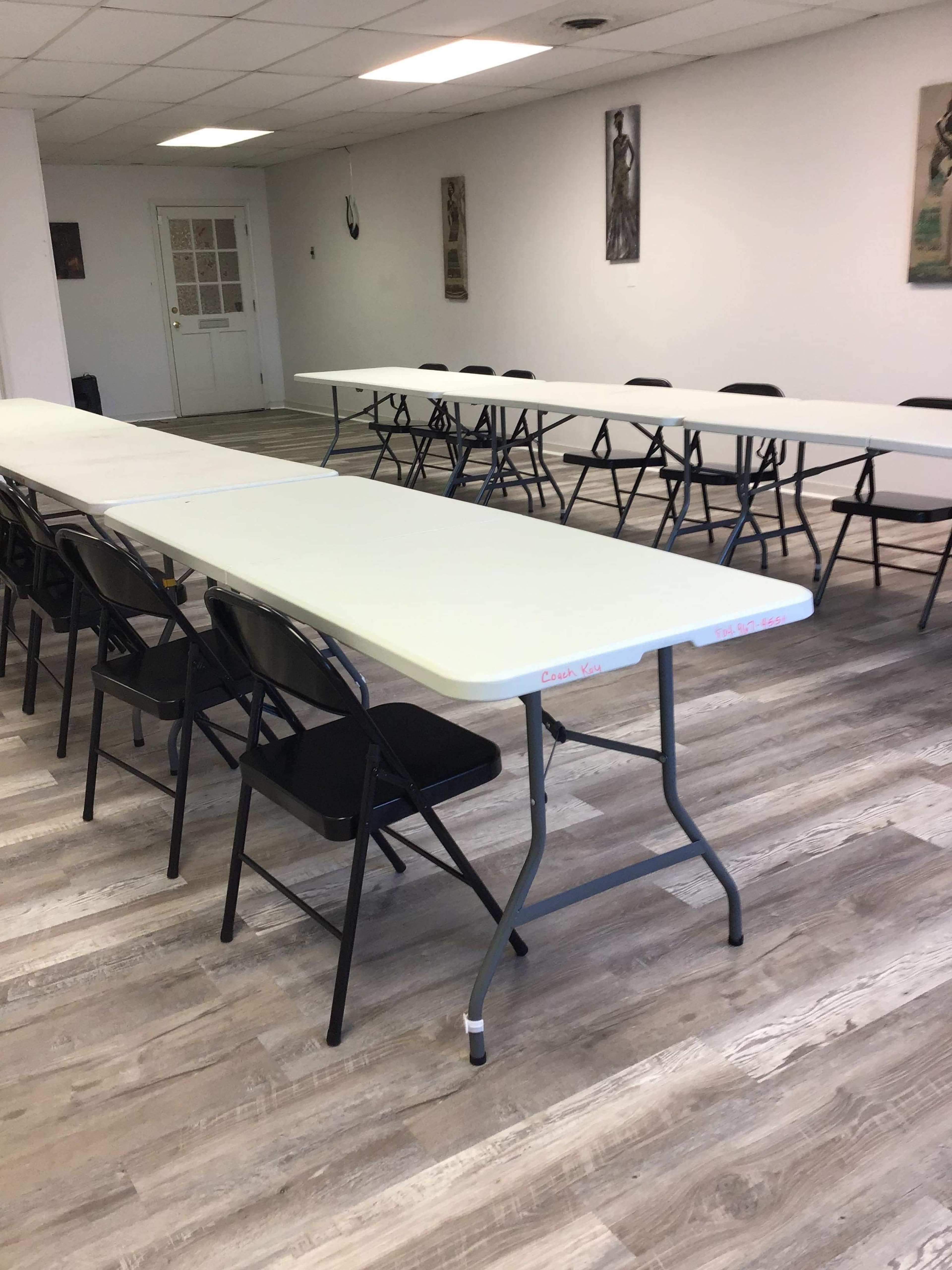 A spacious room features several folding tables arranged in a long, parallel configuration with black chairs lined up on one side.