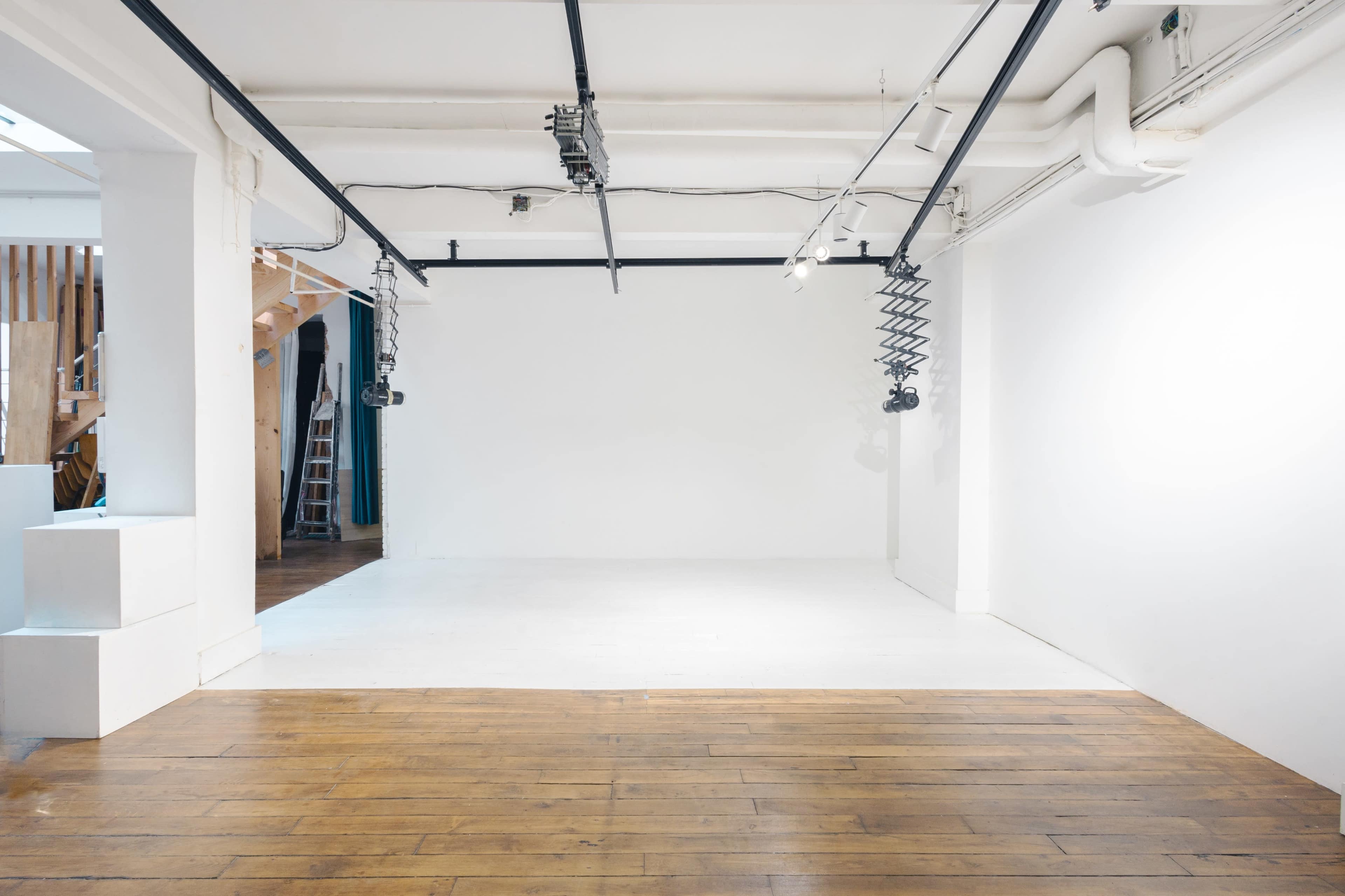 A spacious art gallery with a wooden floor, white walls, and suspended lighting fixtures.