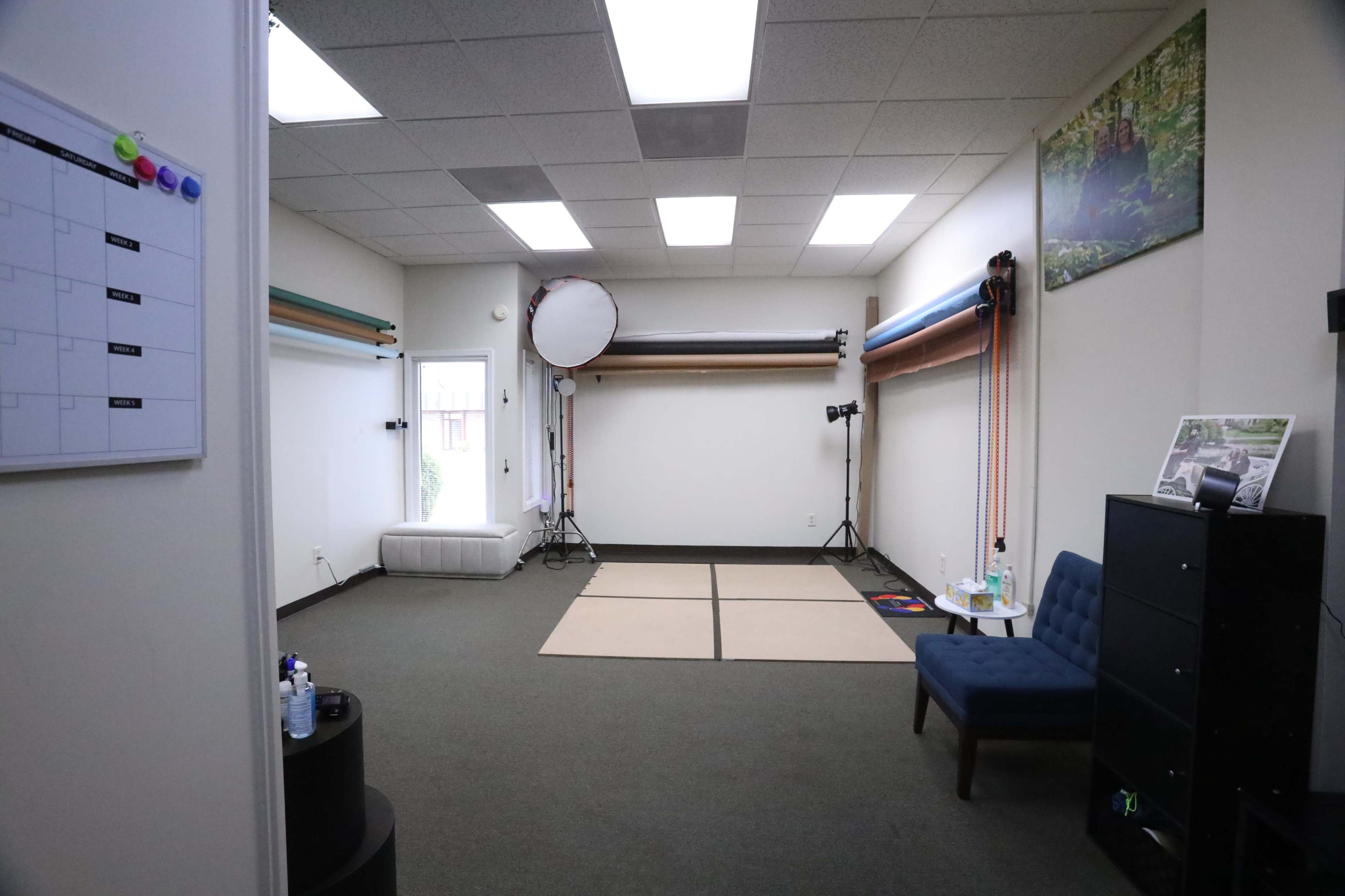 The image shows a studio space with a small seating area, backdrop equipment mounted on the walls, and a large light reflector positioned in the corner.