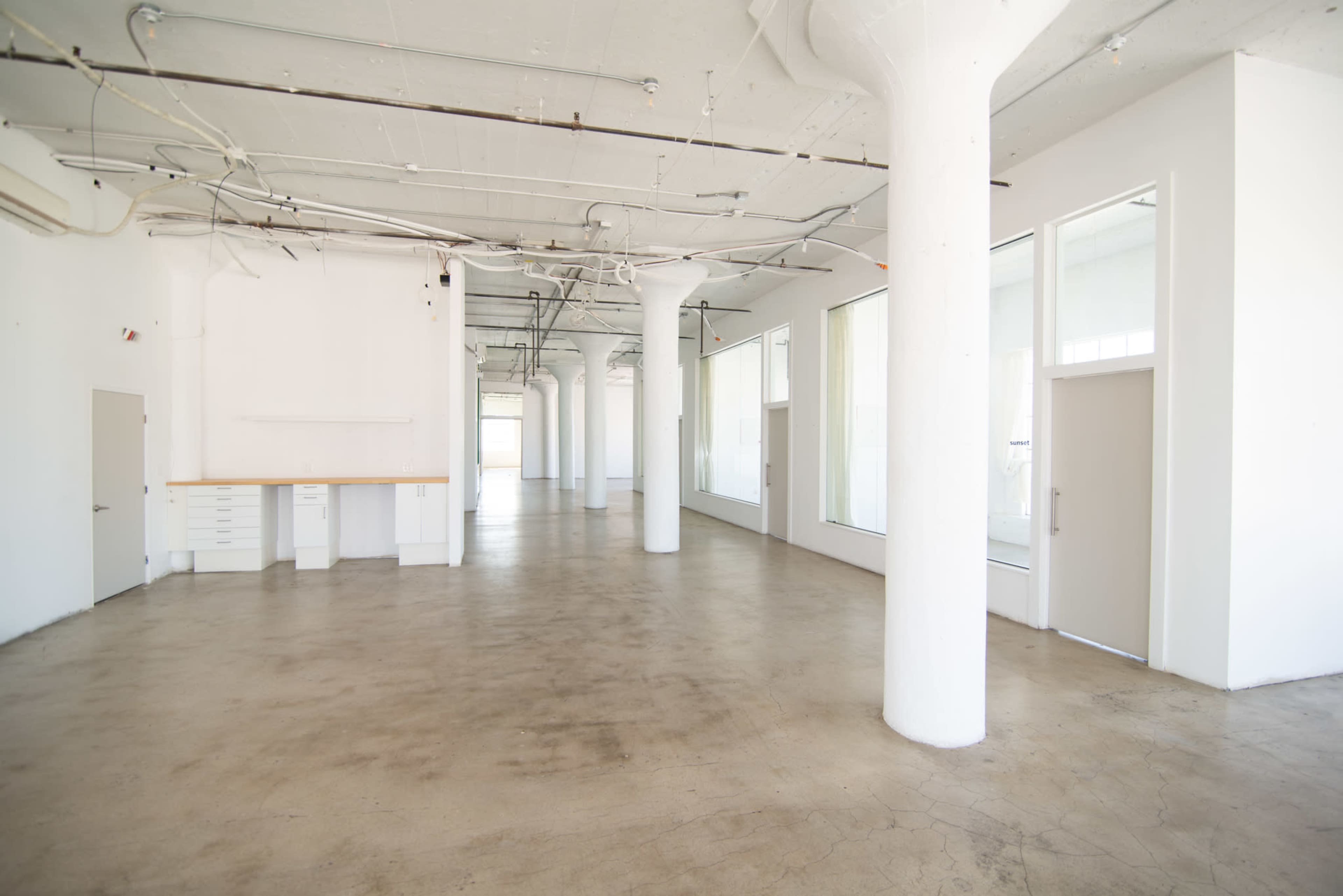 A spacious, empty room with concrete floors, high ceilings, and several large windows.