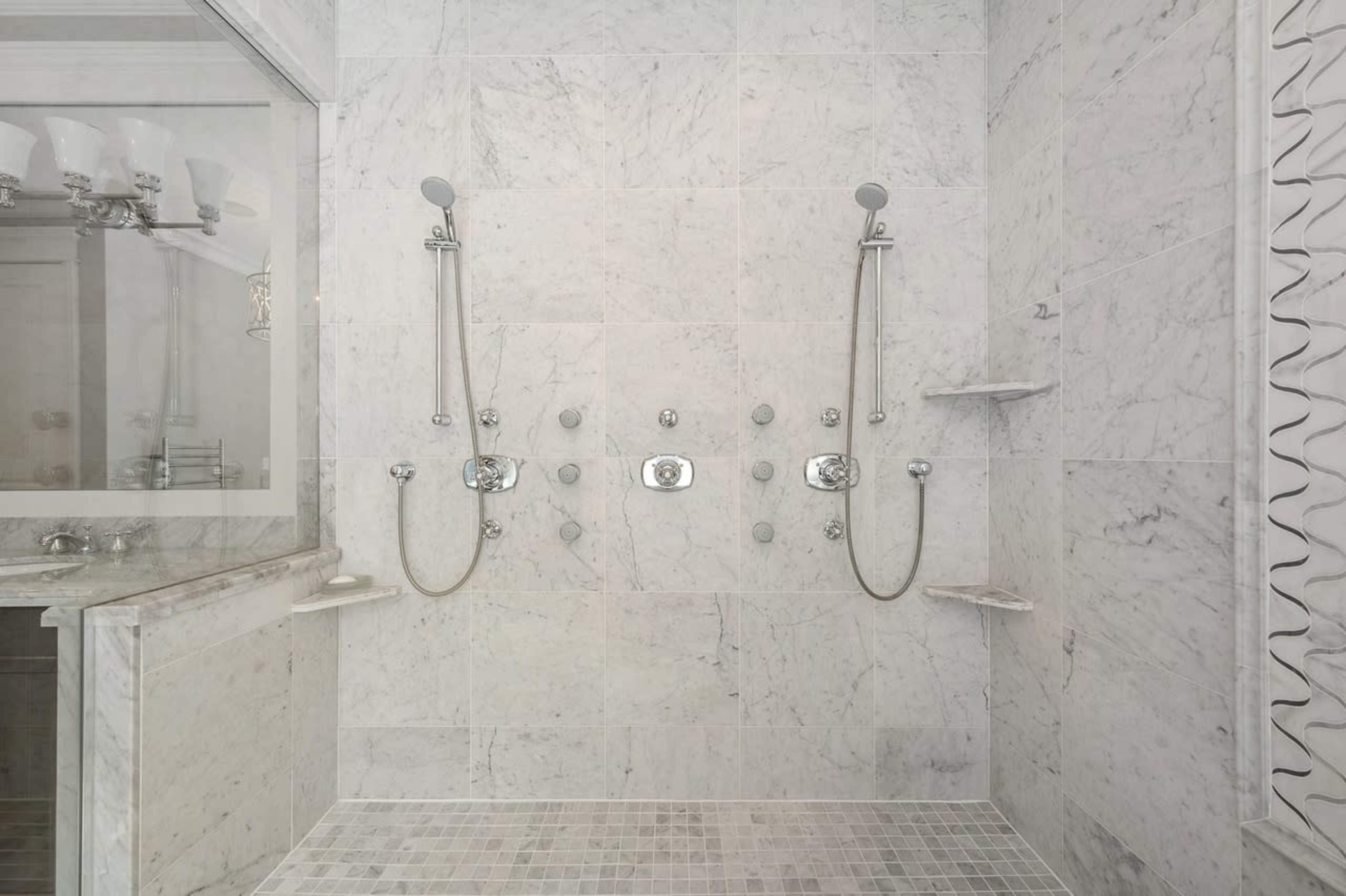 A spacious, modern shower area featuring two showerheads and multiple controls set against a marble wall.