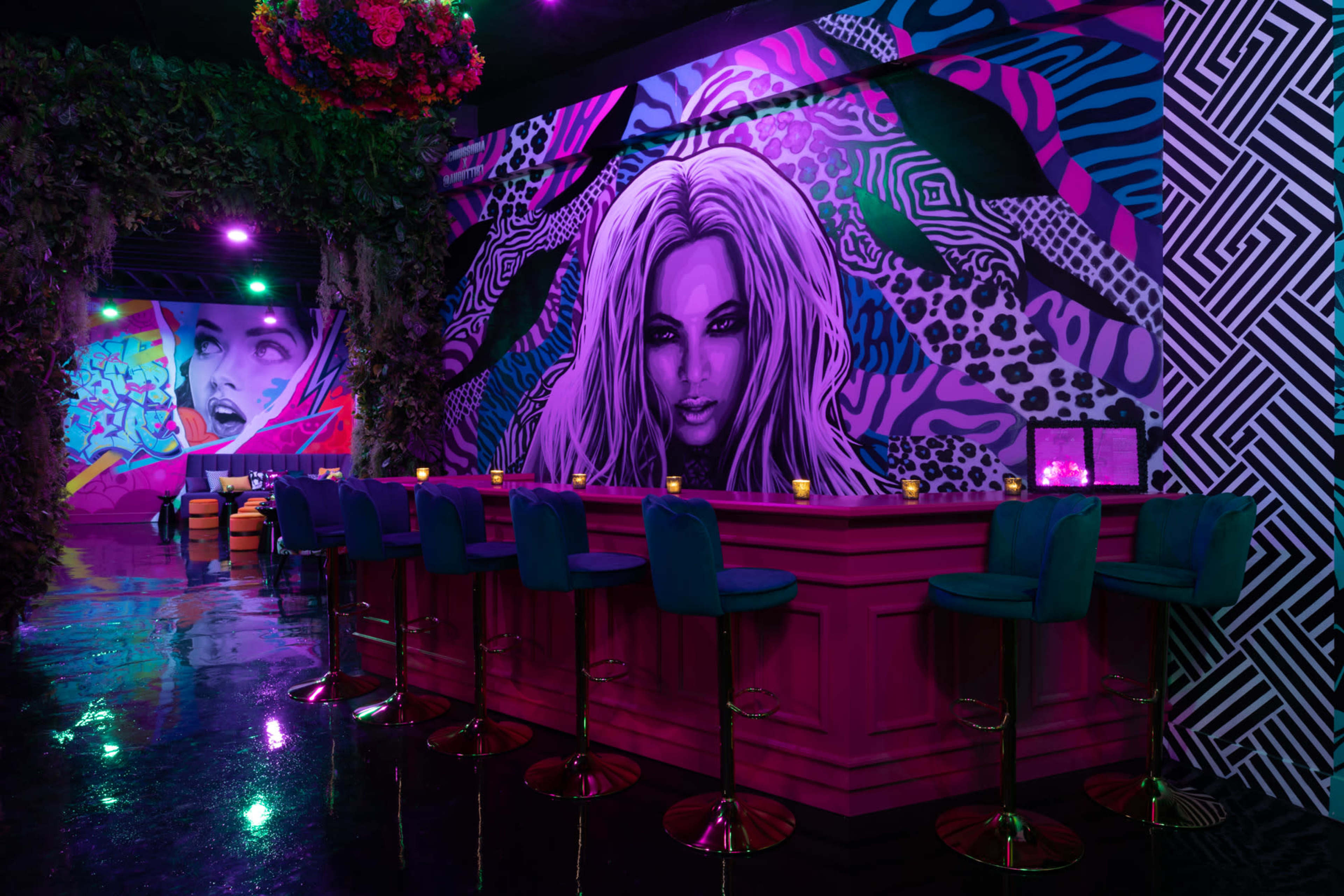 A vibrant bar area features a large mural of a woman's face against a backdrop of bold colors and patterns.