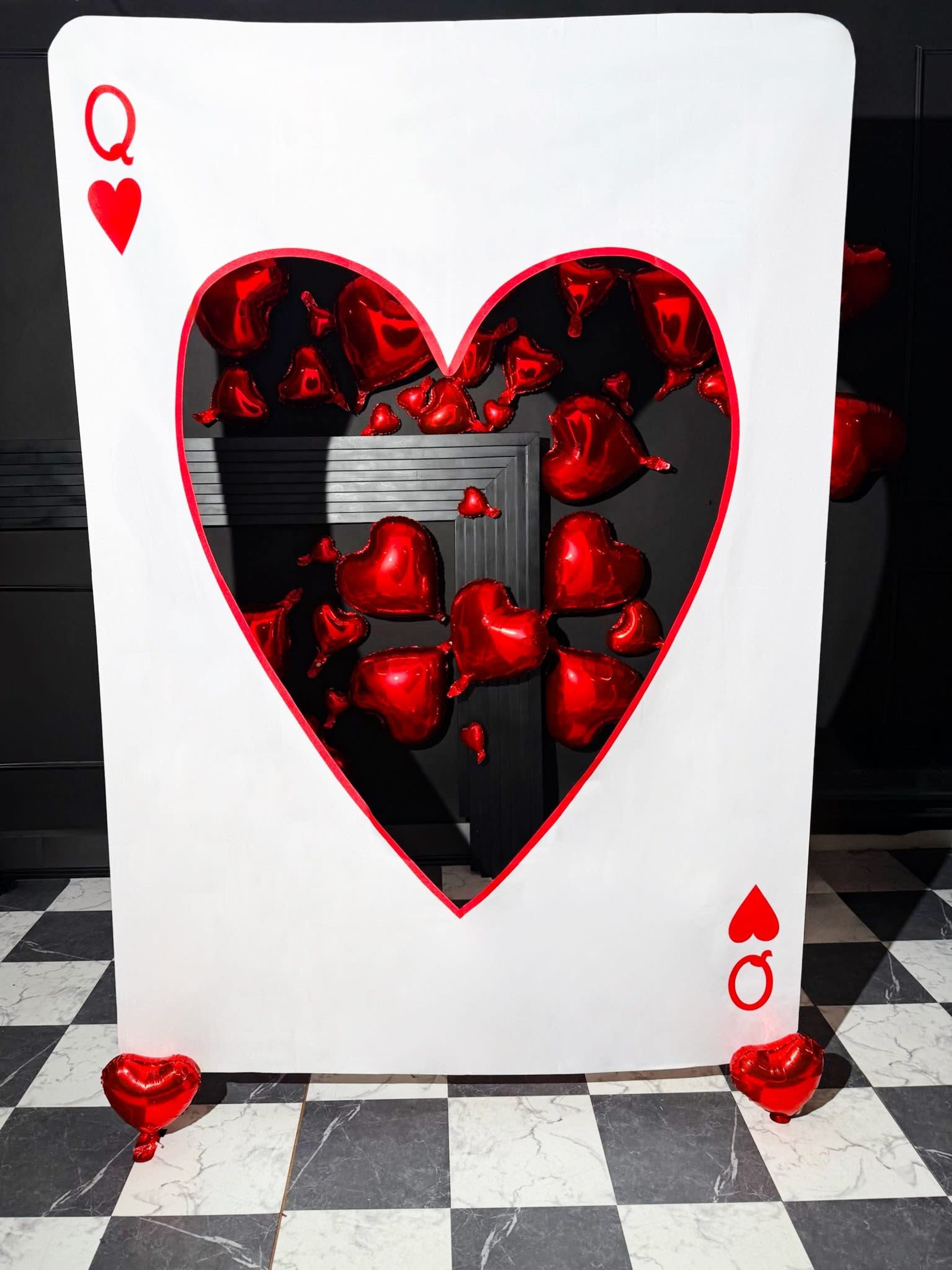 A large, white playing card with a heart cutout features red heart-shaped balloons floating through the opening against a dark background.