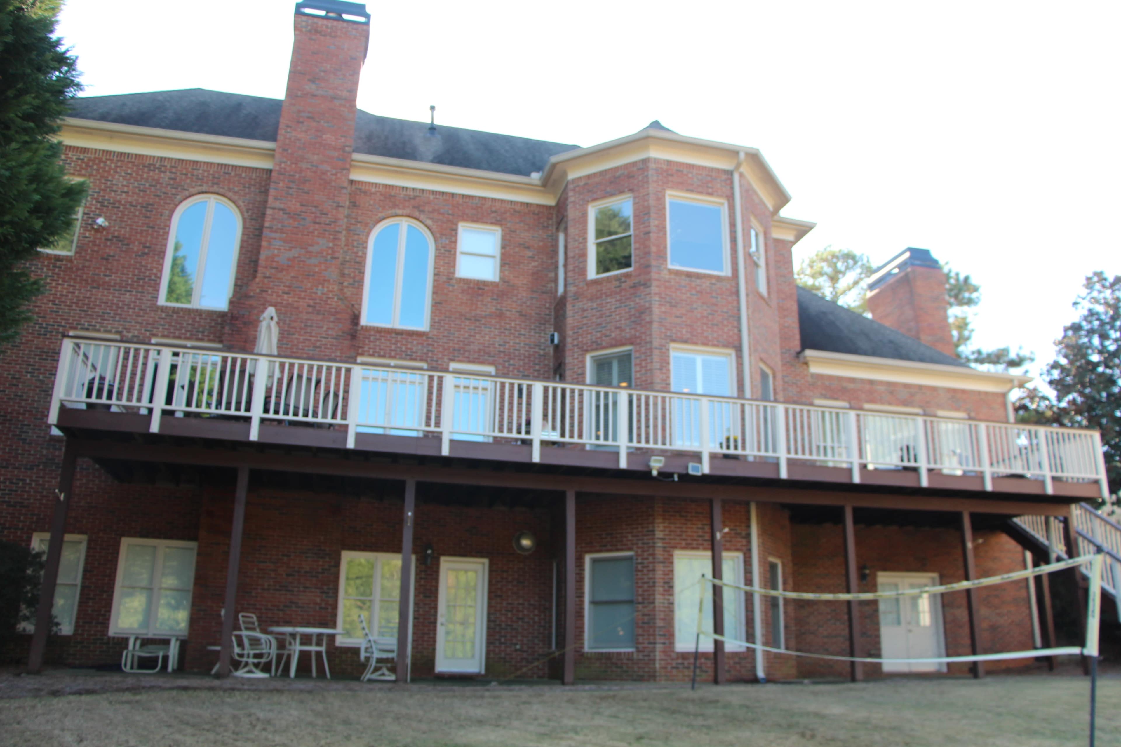 The image shows a two-story brick house with large windows and a wooden deck overlooking a backyard.