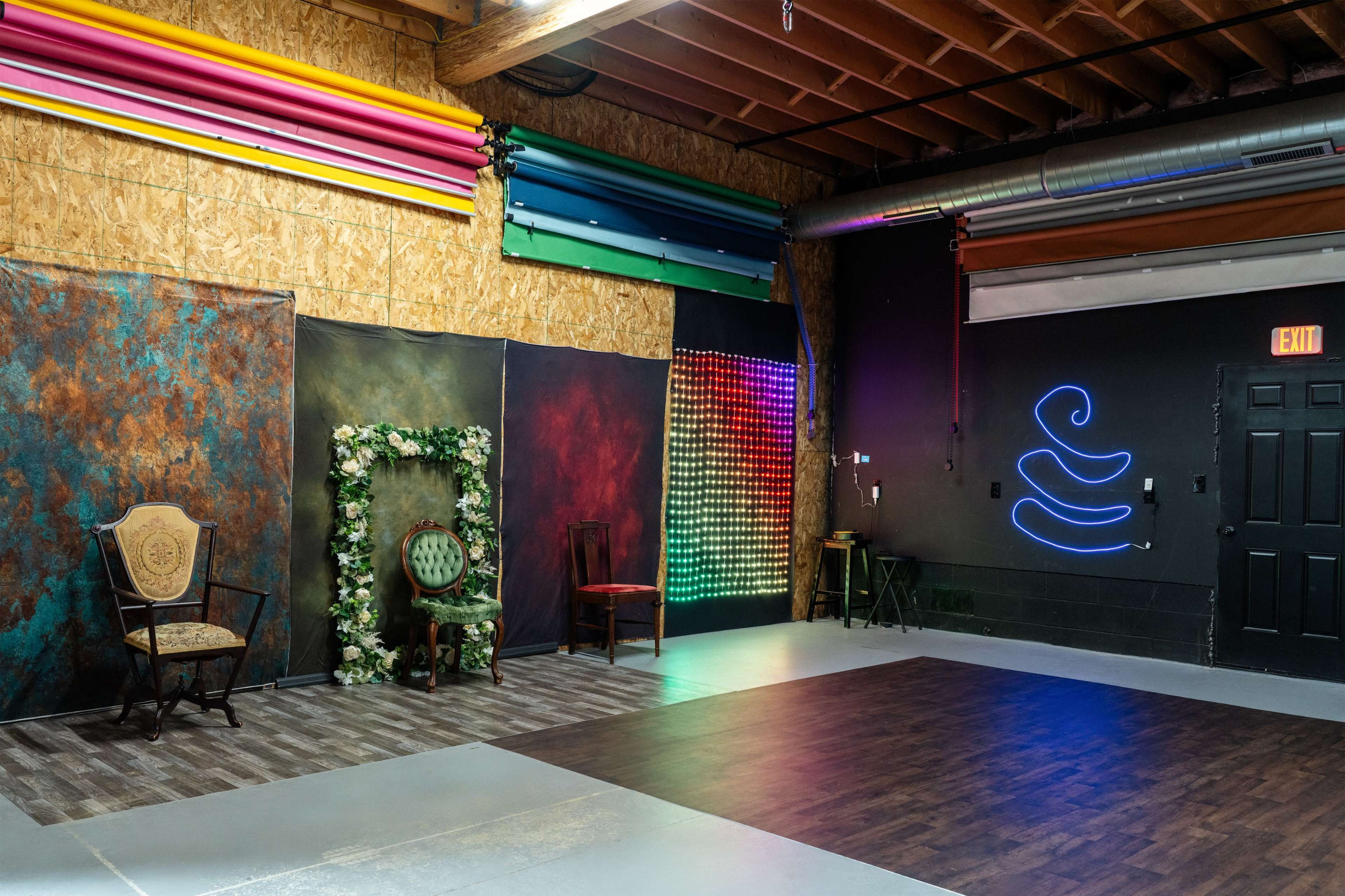 The image shows a spacious room with an artistic background, featuring a decorative frame with flowers, a green chair, and a colorful LED light display on one wall.
