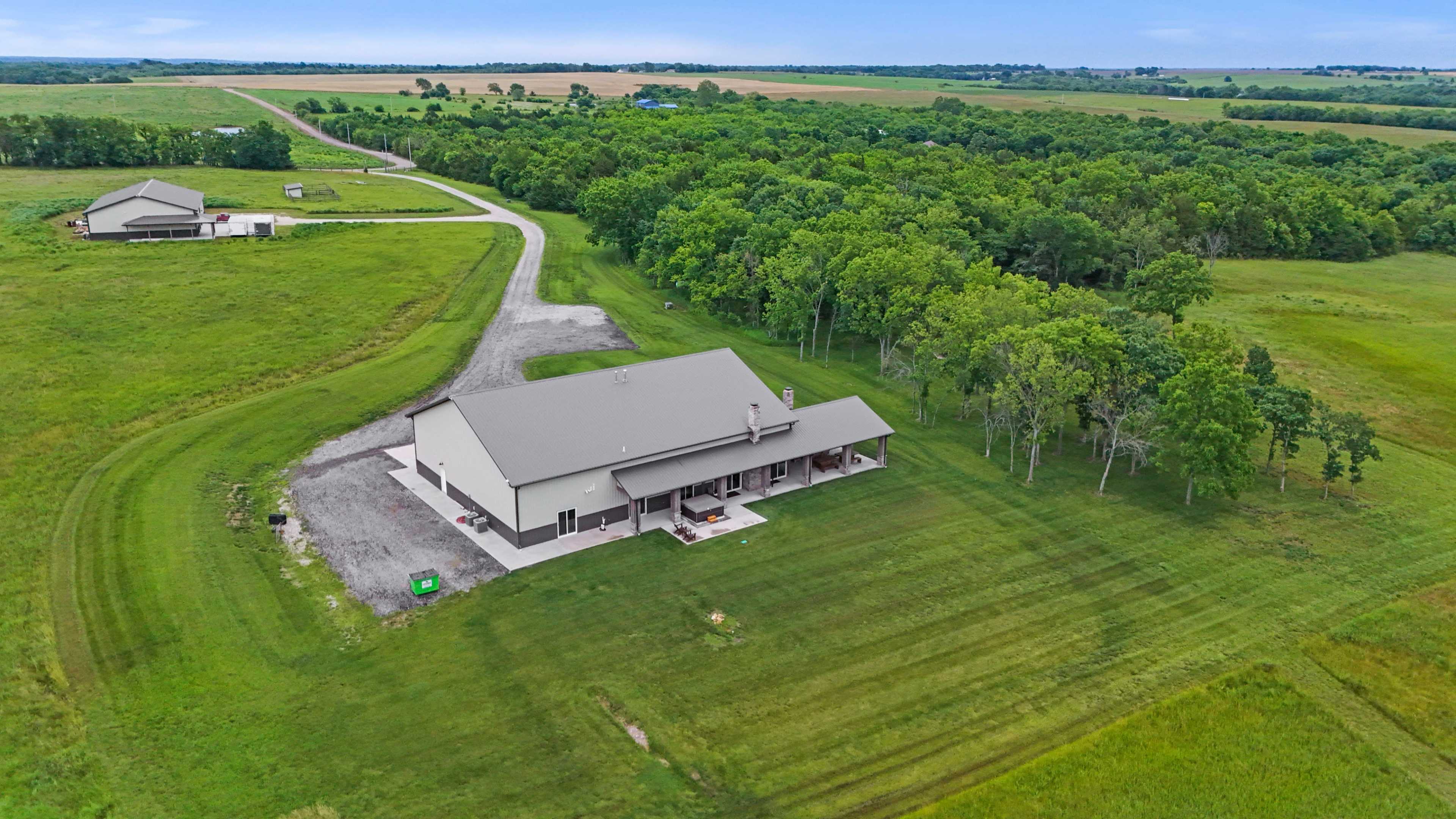 The image shows a large, single-story building surrounded by grassy fields and trees, with a winding road leading to it from the background.