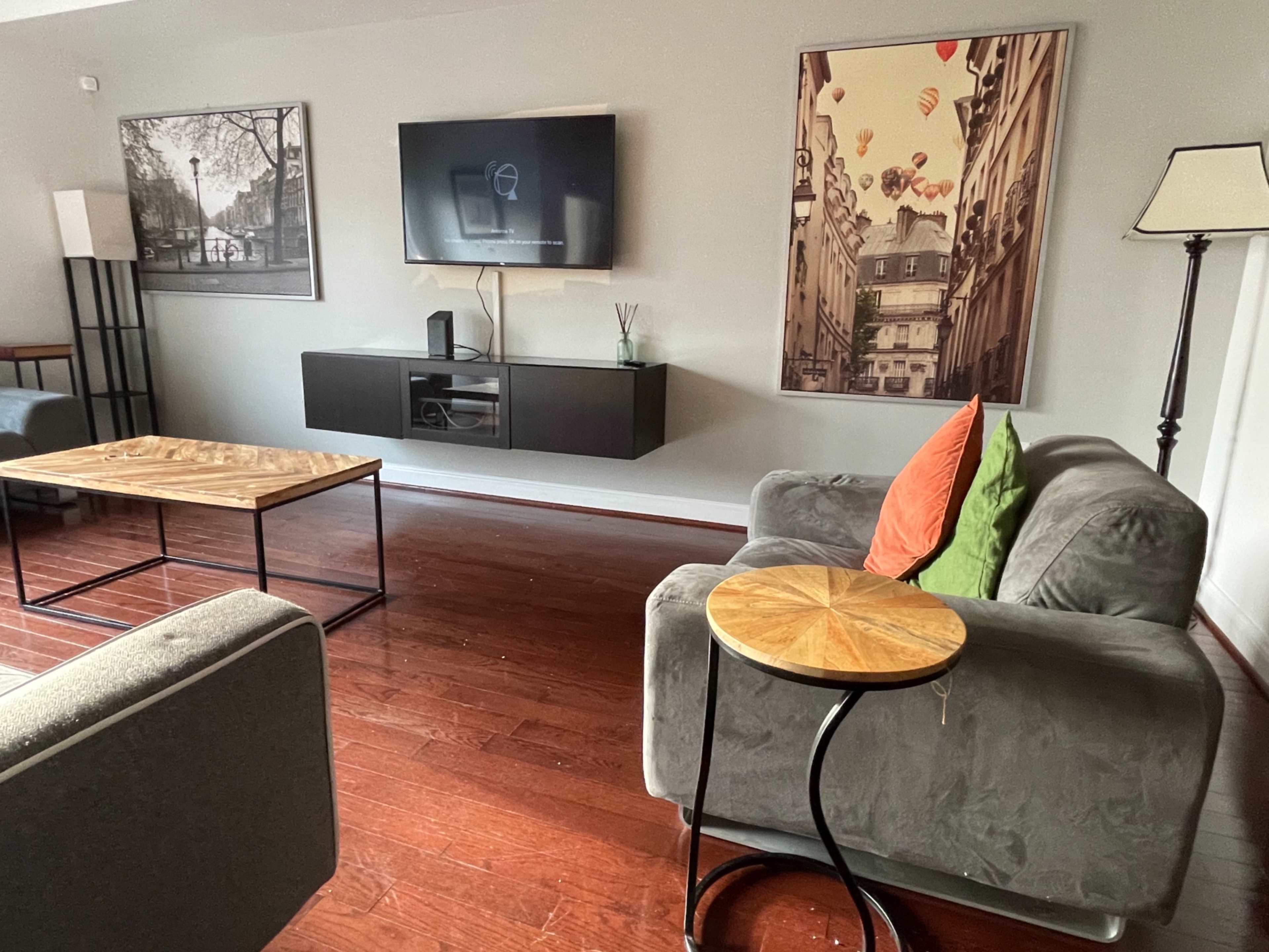 A modern living room with two sofas, a small round side table, a television mounted on the wall, and framed artwork on display.
