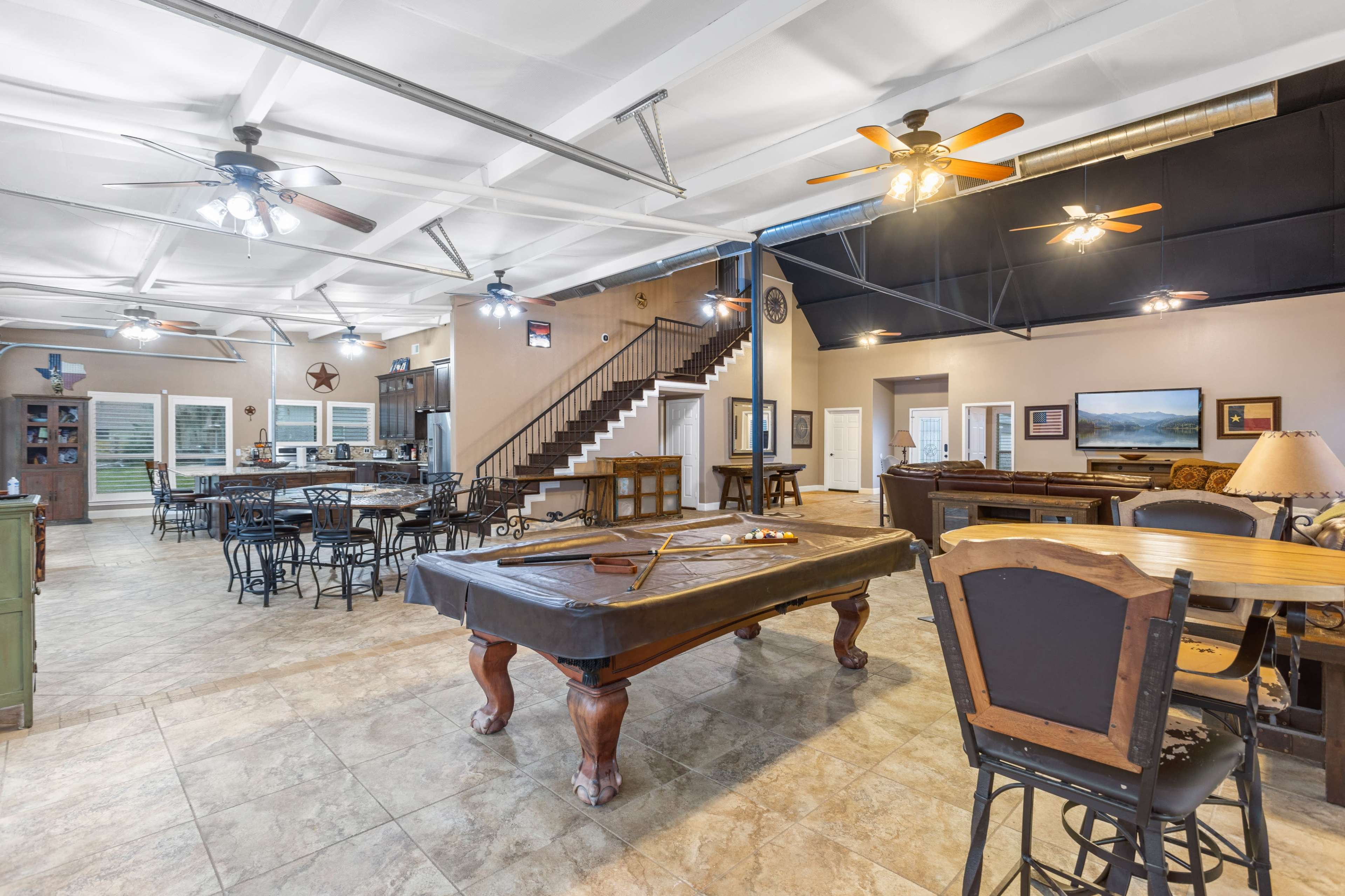 A large, open space featuring a billiard table, dining tables, and a staircase in a well-lit, multi-purpose room.