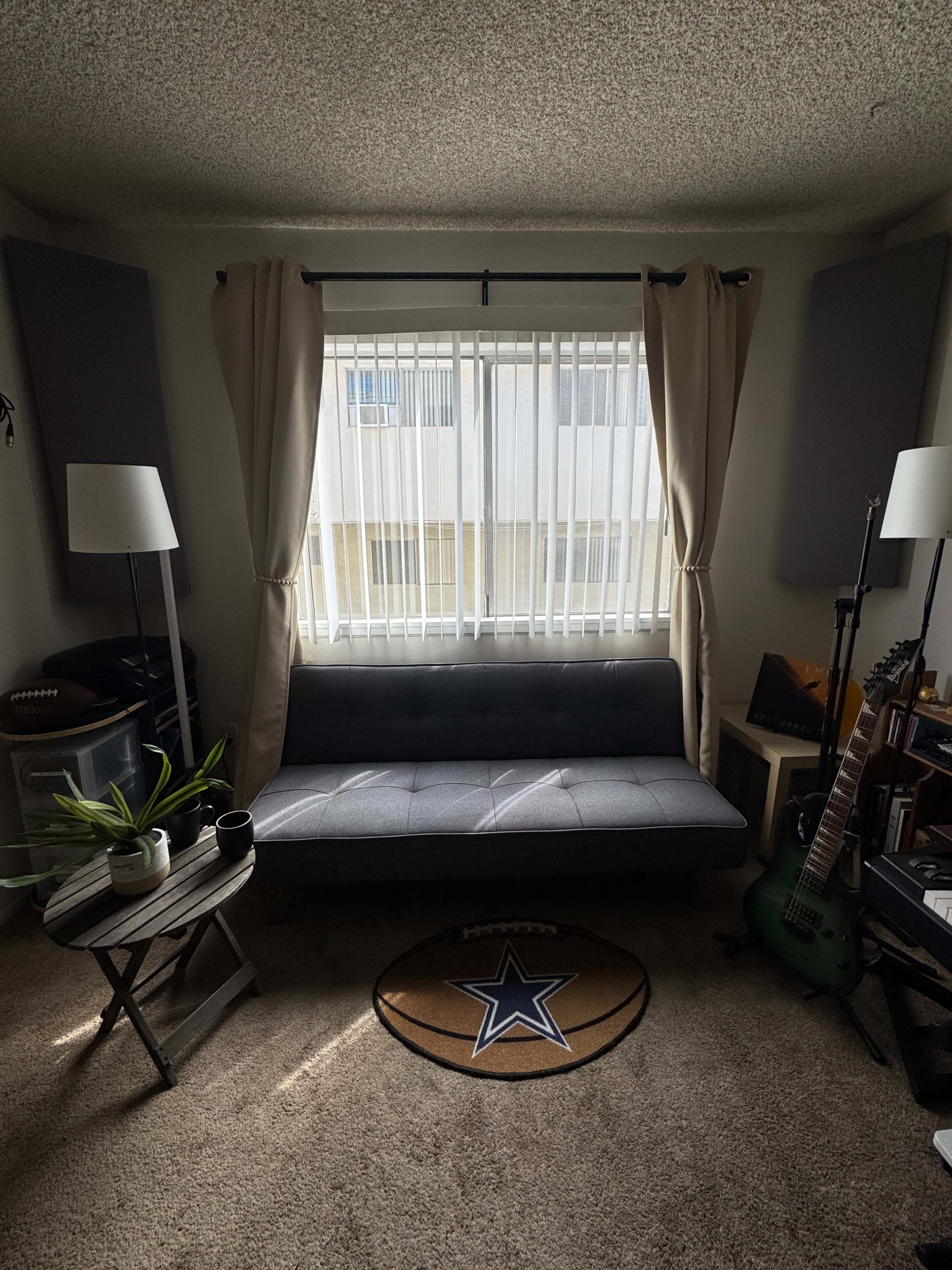 The scene shows a small living space with a gray futon, a round basketball-themed rug, two floor lamps, and a guitar leaning against a shelf.