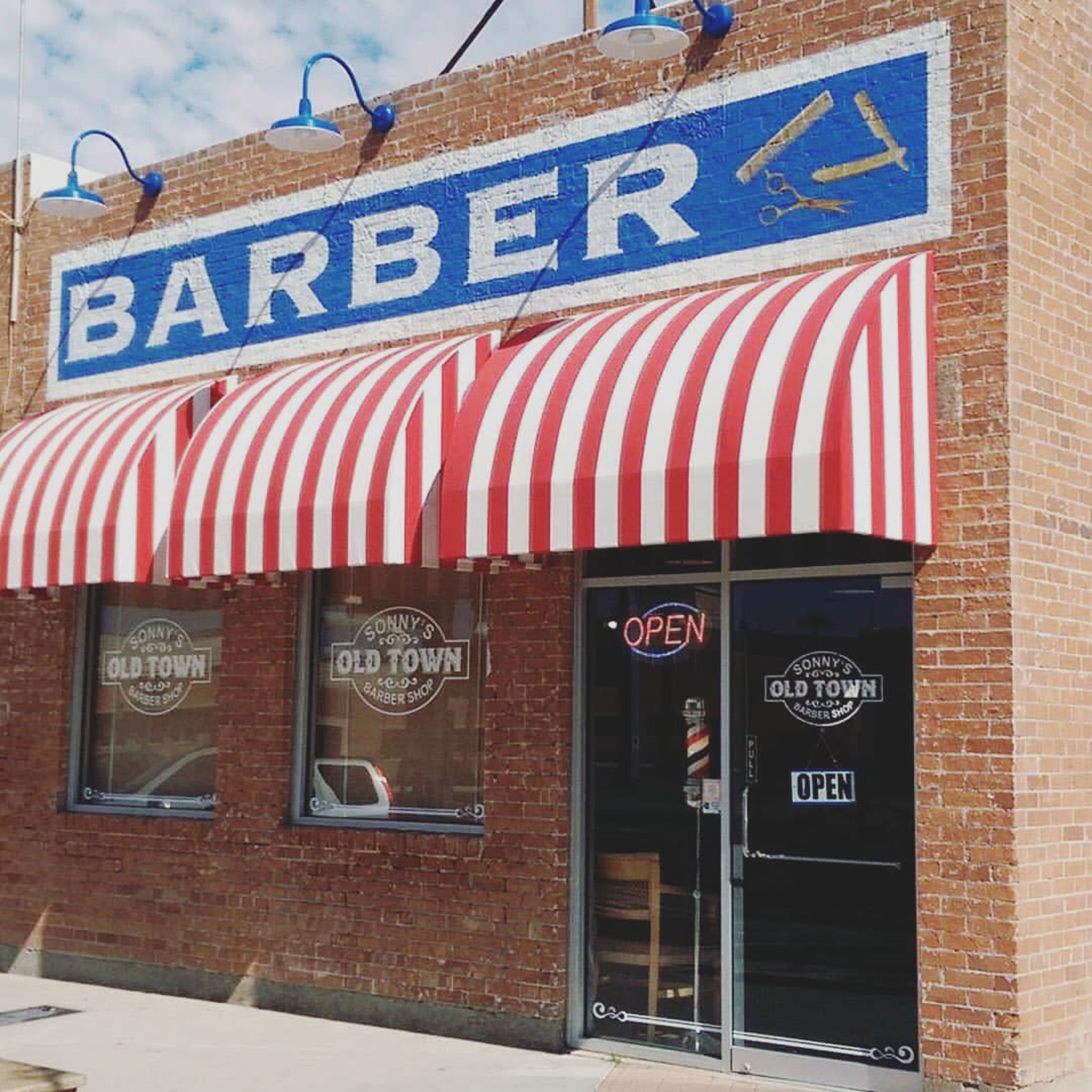 A brick building with an awning featuring red and white stripes and a sign that reads "BARBER" in blue letters.