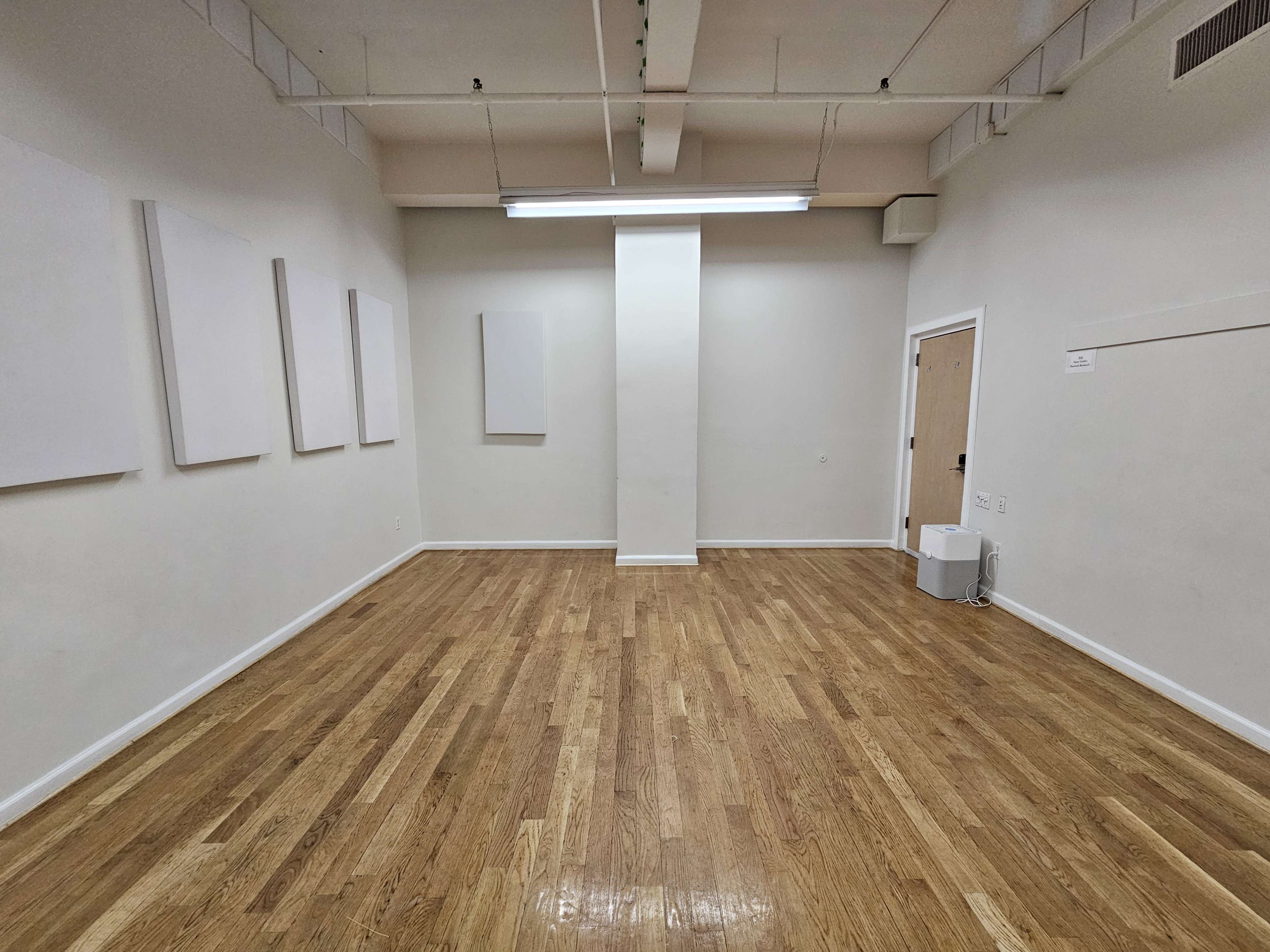 A spacious, empty room with wooden floors and white walls features several blank canvases hung on one side.
