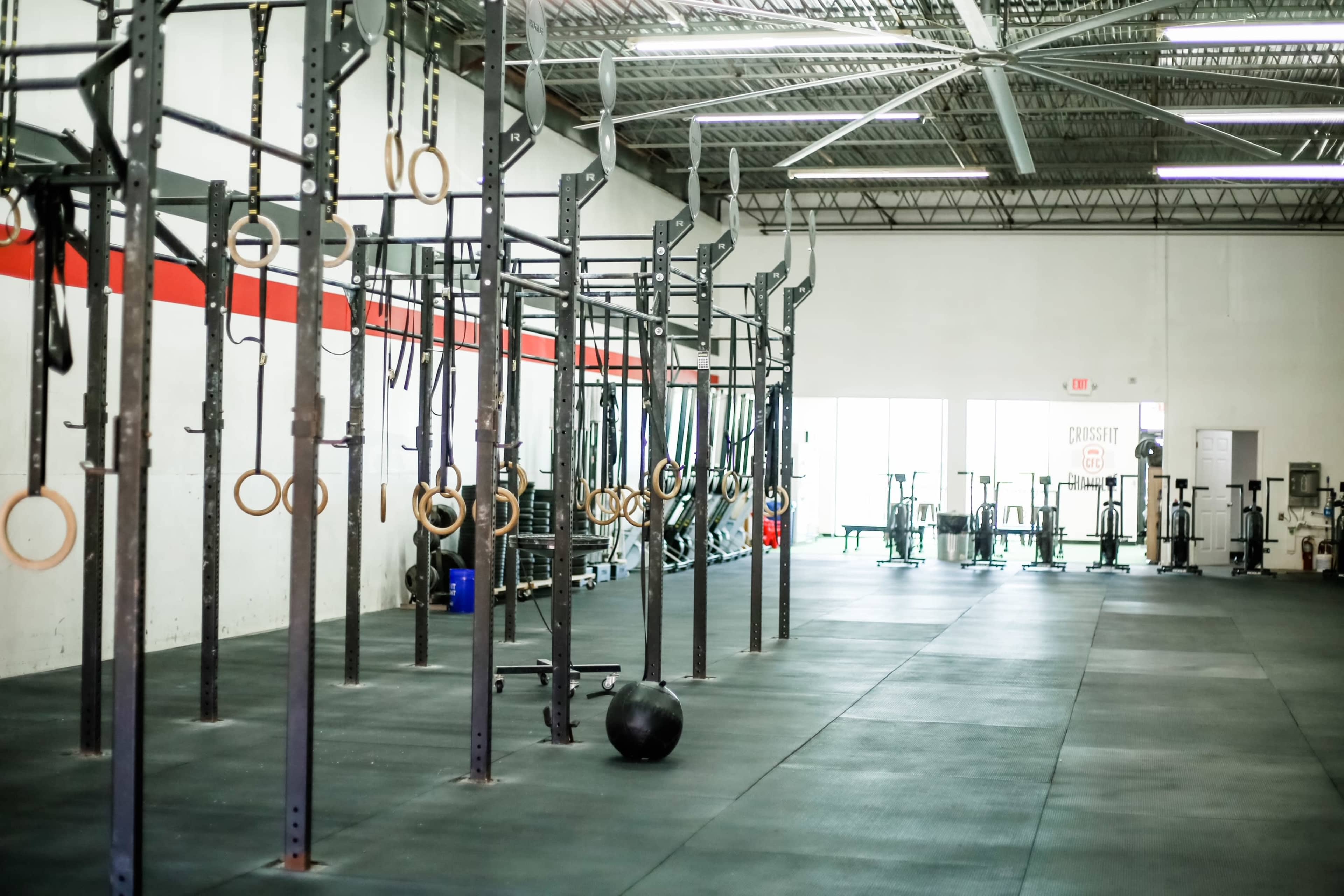 A spacious gym with rows of pull-up bars and gymnastic rings against a white wall, and a large rubber mat area.