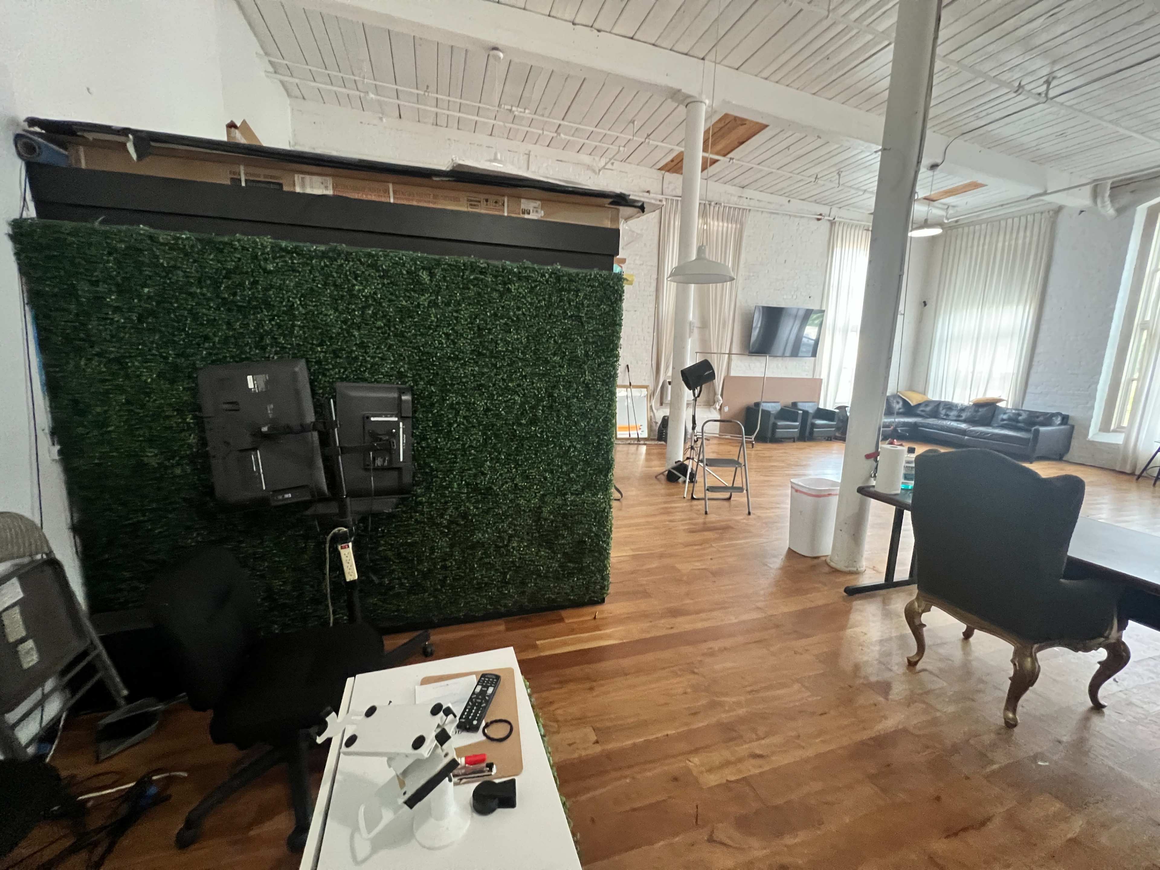 The image shows a spacious room featuring a green artificial hedge wall, desk equipment, and various seating areas.