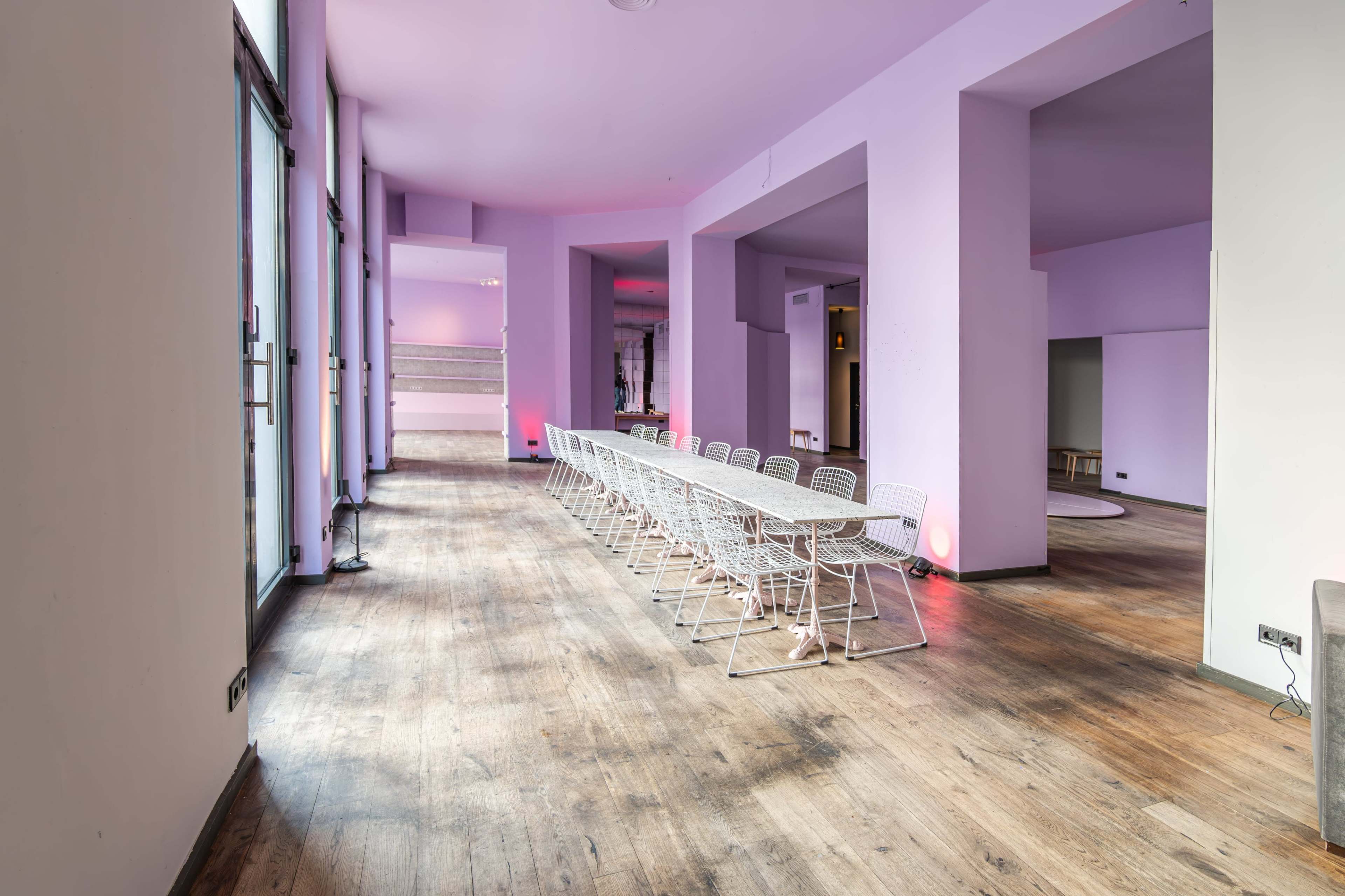 A large, empty room features a long table set with white chairs, complemented by purple walls and wooden flooring.