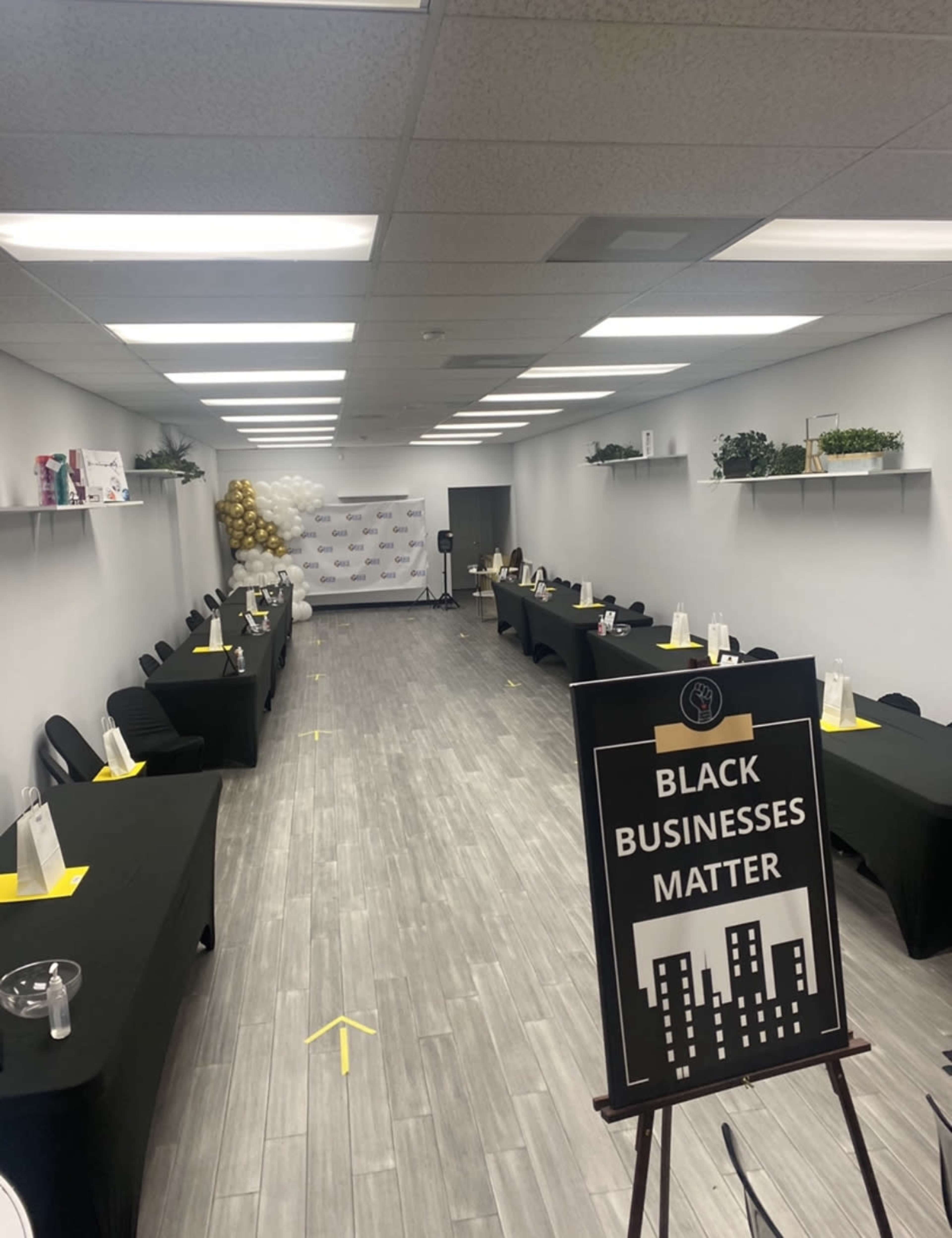 A spacious, well-lit event room set up with black tables and chairs, featuring a sign that reads "BLACK BUSINESSES MATTER" in the foreground.