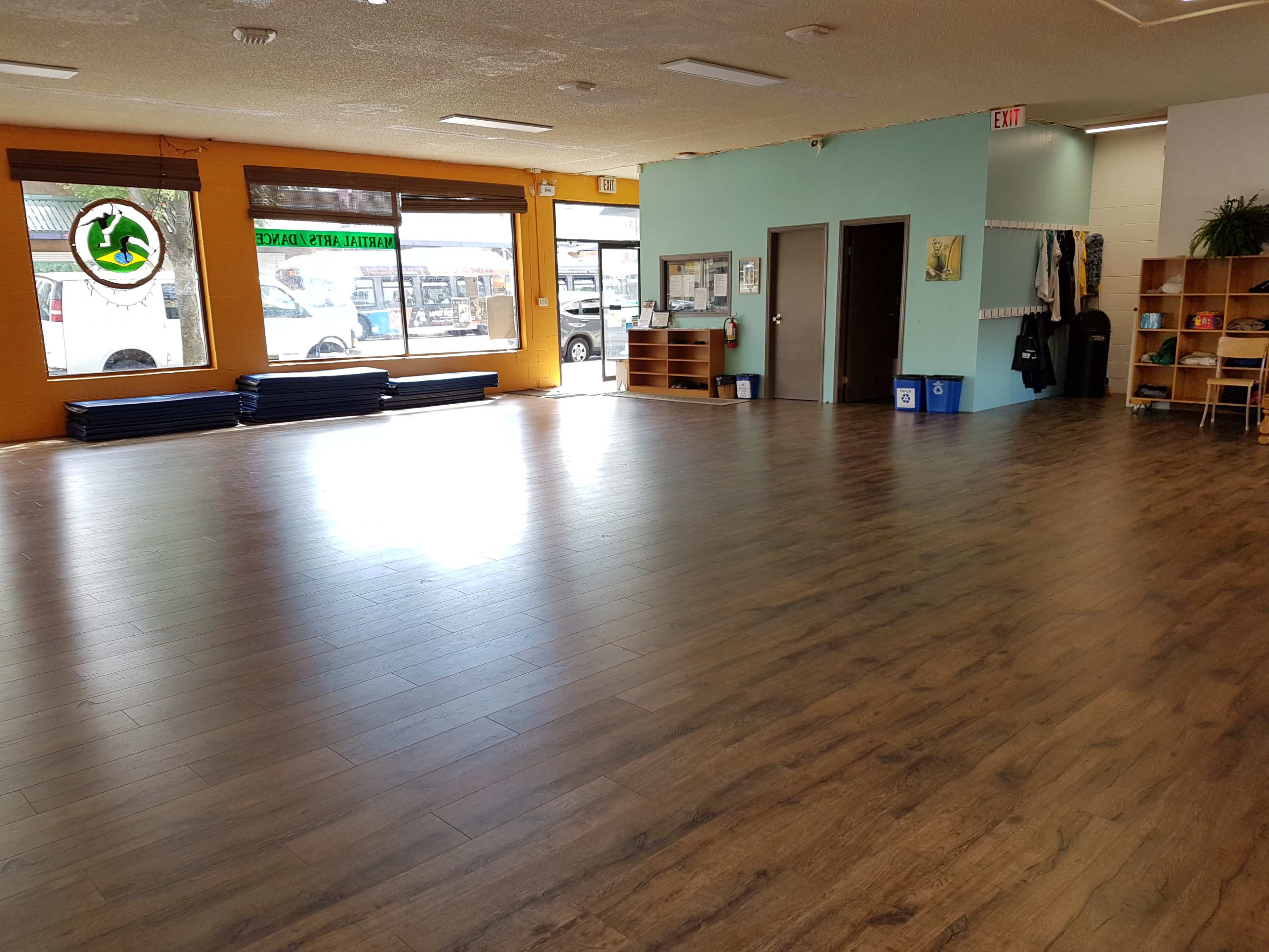 A spacious, empty room with wooden flooring, large windows, and a small reception area on the right.