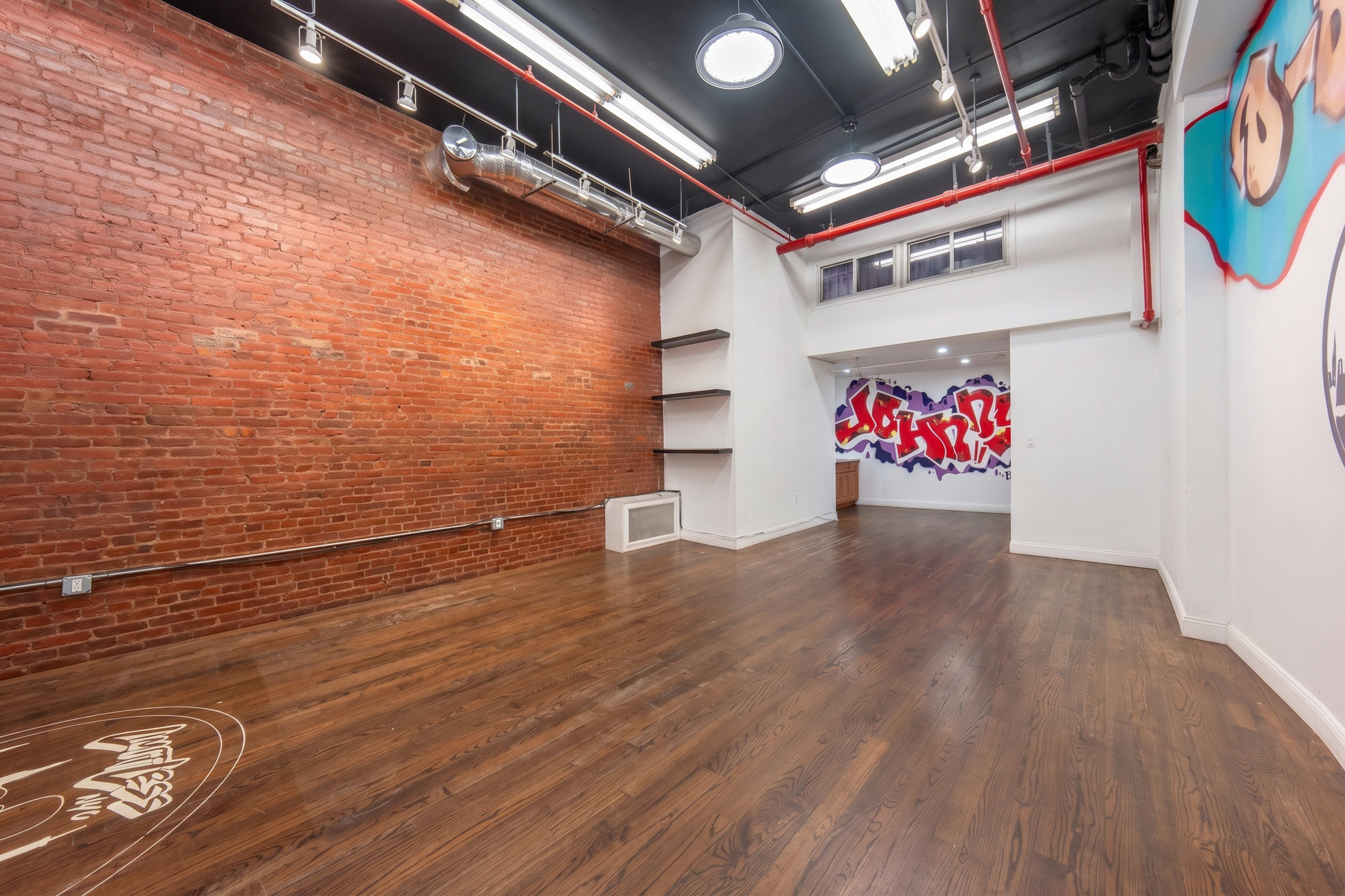 The image shows an interior space with exposed brick walls, hardwood floors, and a mural on one wall, featuring graffiti-style art.
