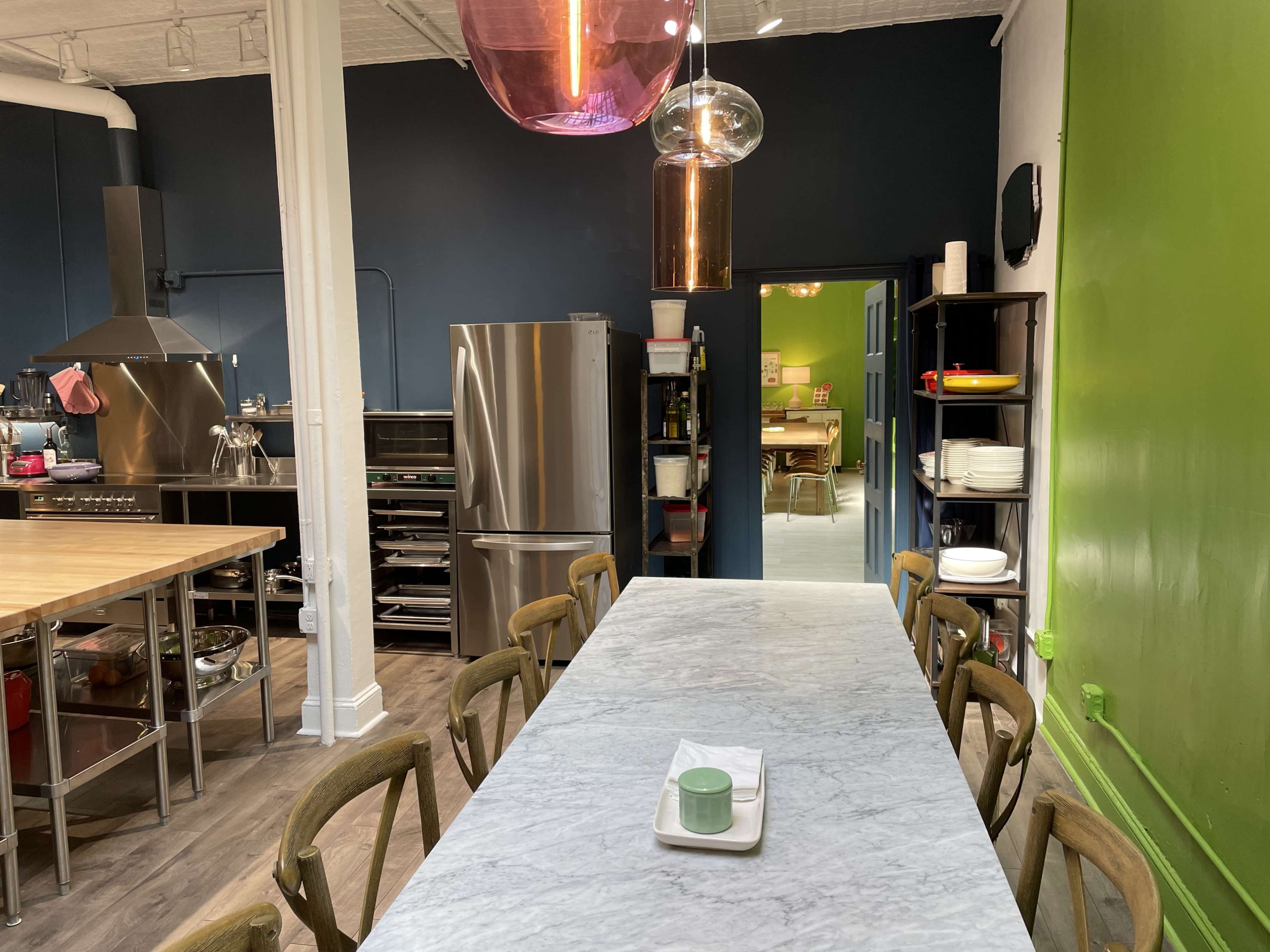 A spacious kitchen features a long marble table, stainless steel appliances, and vibrant green and blue walls.
