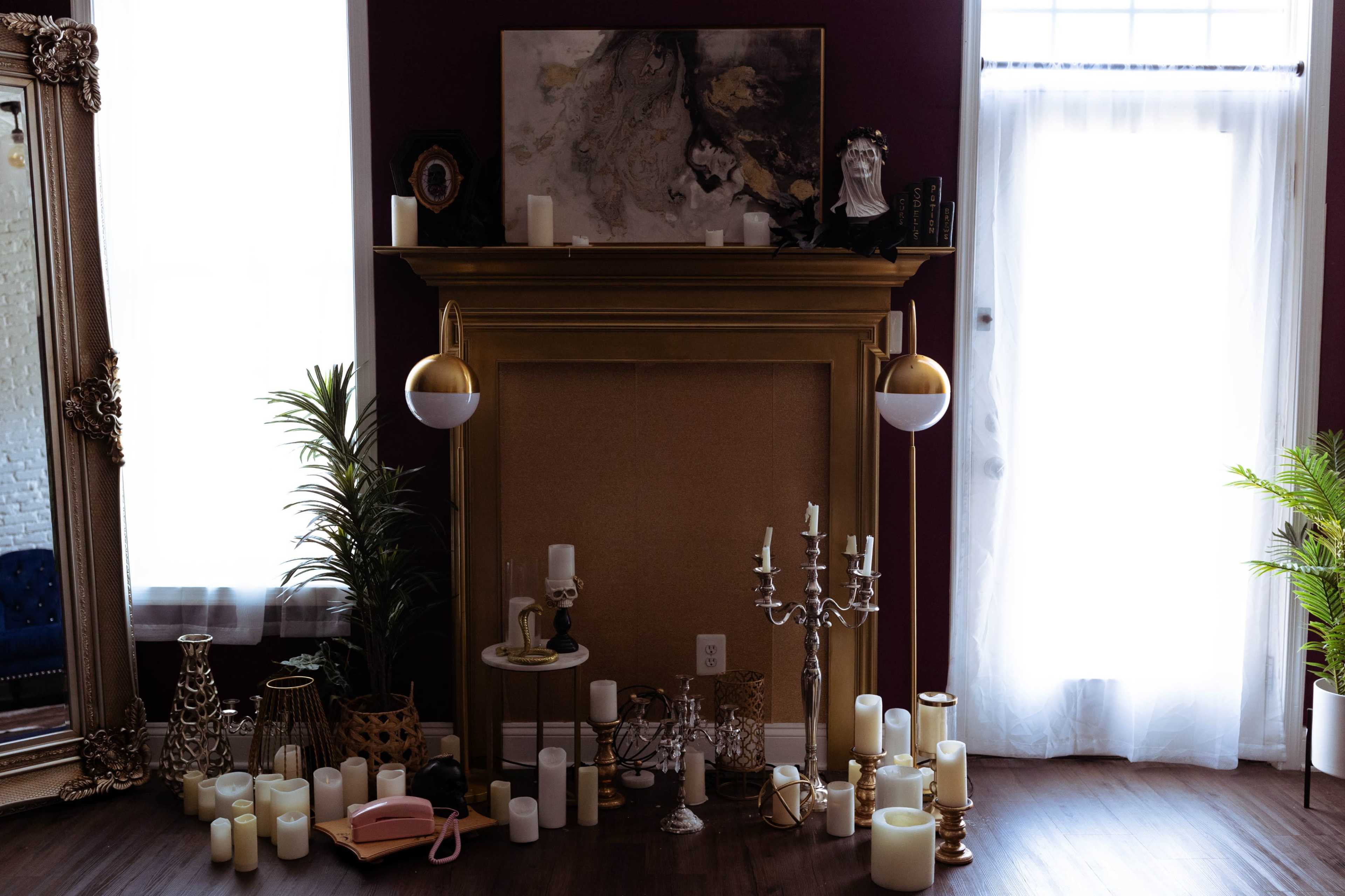 A room with a gold-framed mirror, a fireplace adorned with various candles and decorative items, and a large window letting in natural light.
