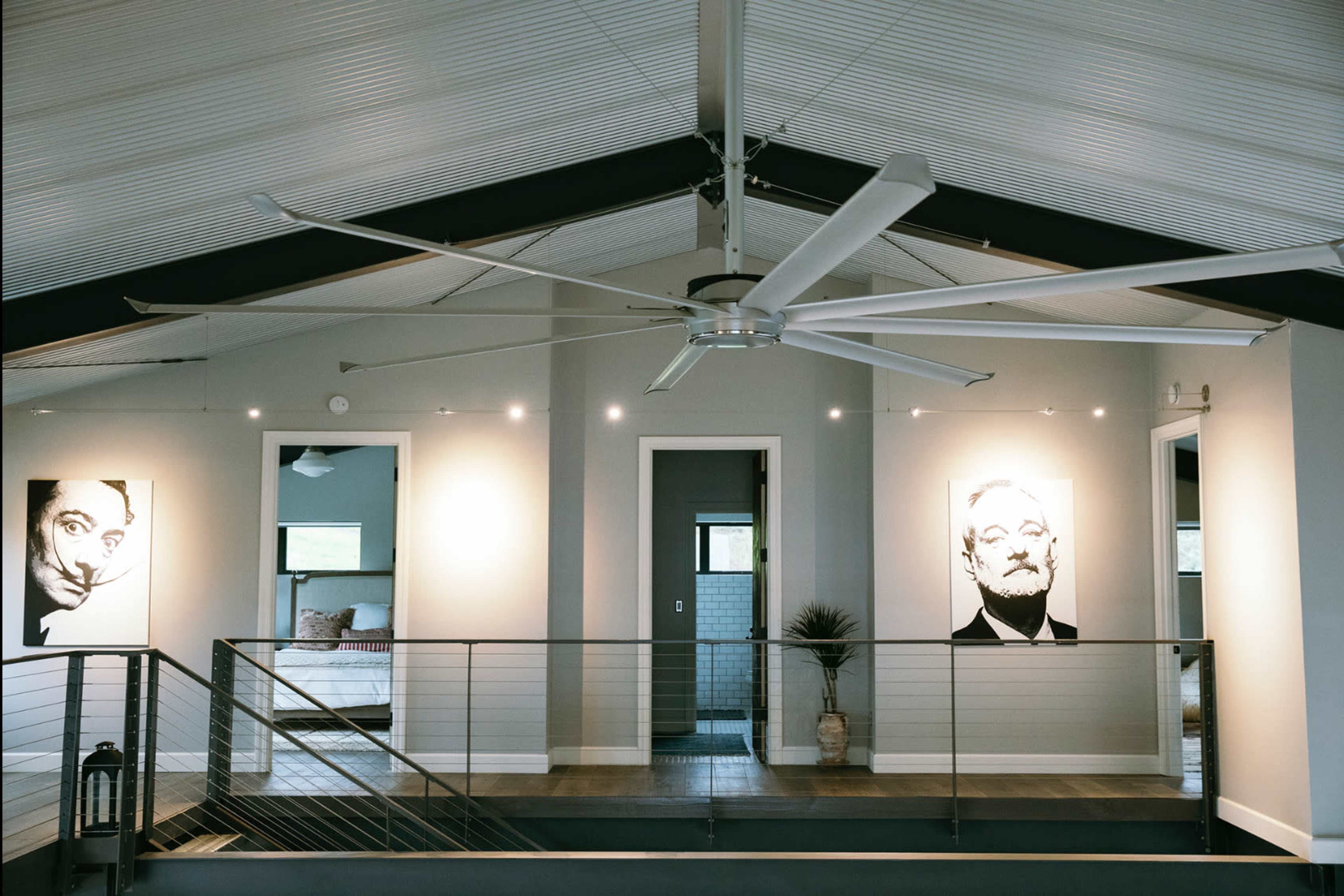 The interior of a modern loft features a high ceiling, a large ceiling fan, and two portraits on the walls, with doorways leading to additional rooms in the background.