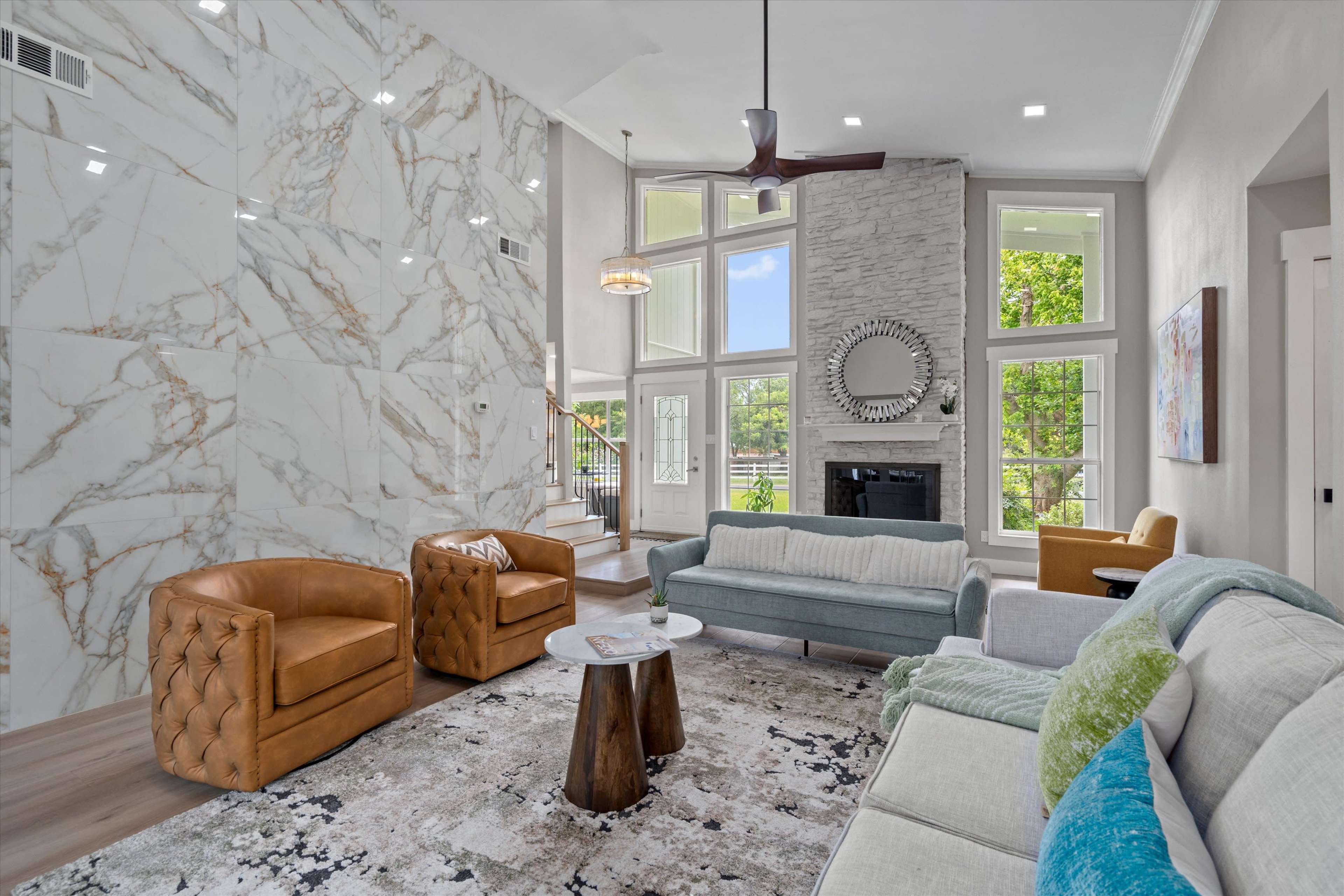 A spacious living room features a marble accent wall, large windows, and a combination of modern seating arrangements.
