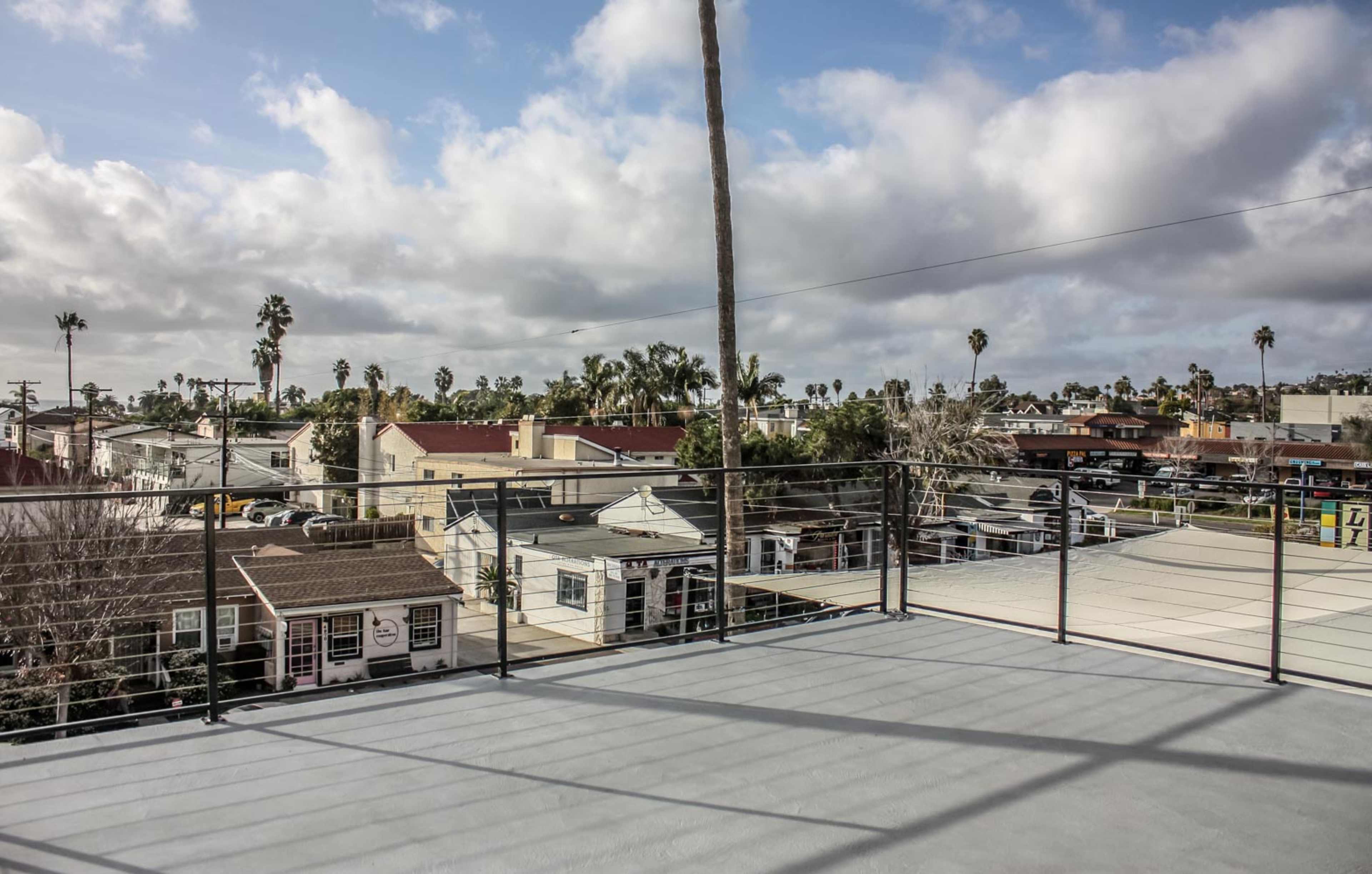 A rooftop deck overlooking a neighborhood with houses, palm trees, and cloudy skies in the background.
