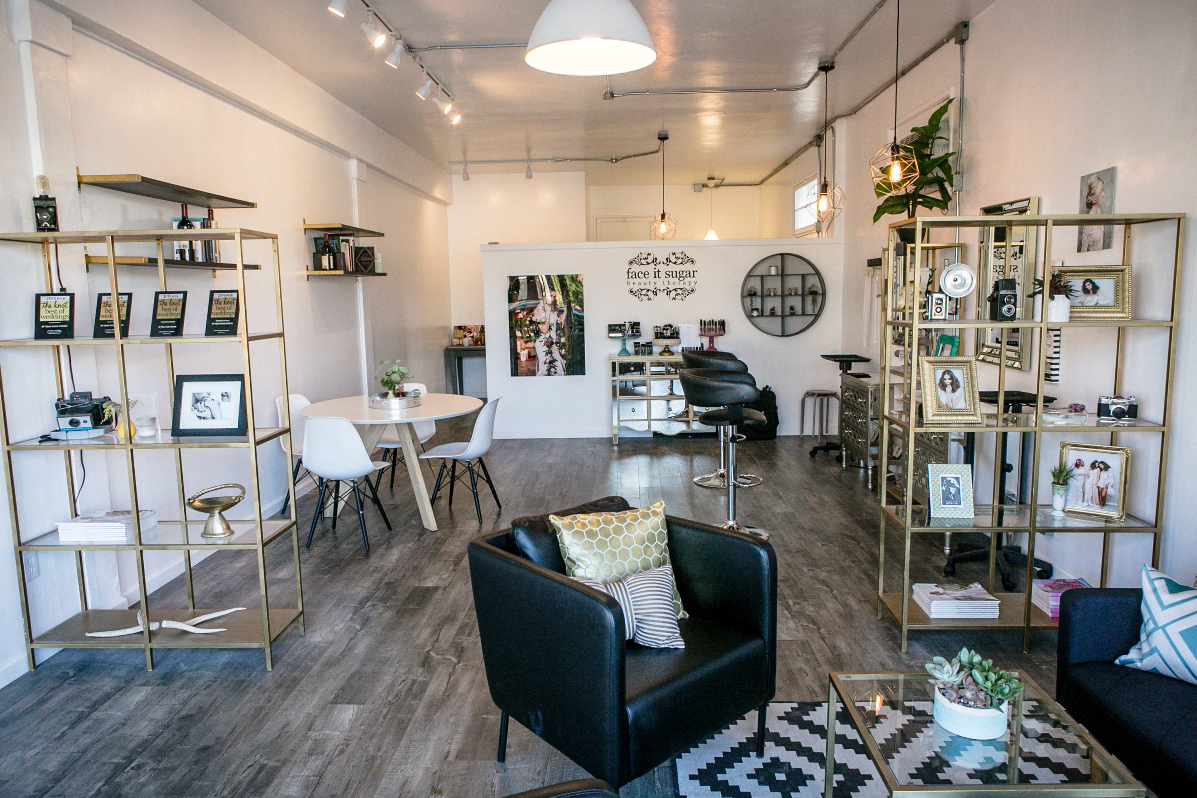 The image shows a modern, open space with wooden flooring, featuring stylish furniture, bookshelves, and decorative elements.