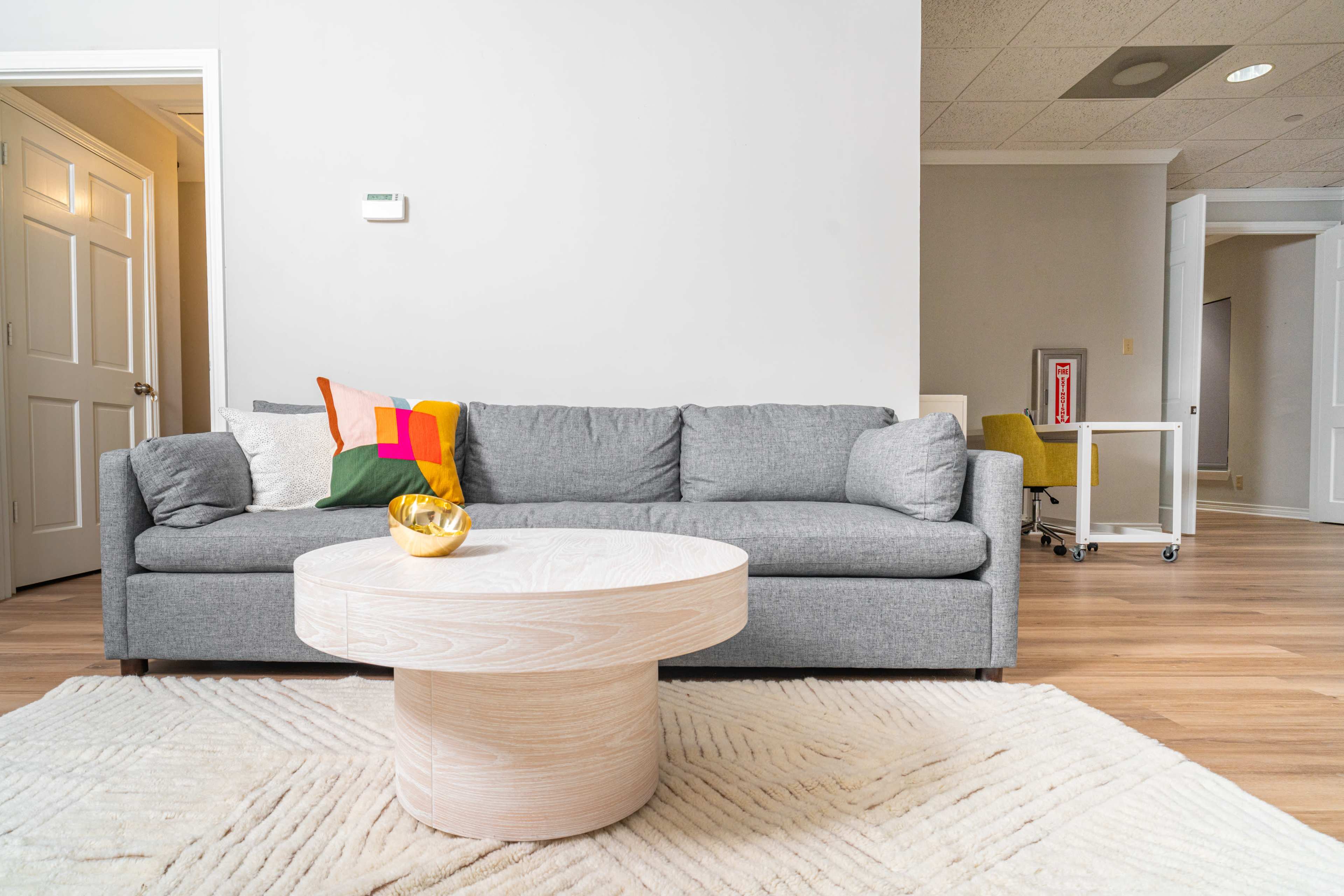 A gray sofa sits in a bright, modern living space with a round wooden coffee table on a light-colored rug.