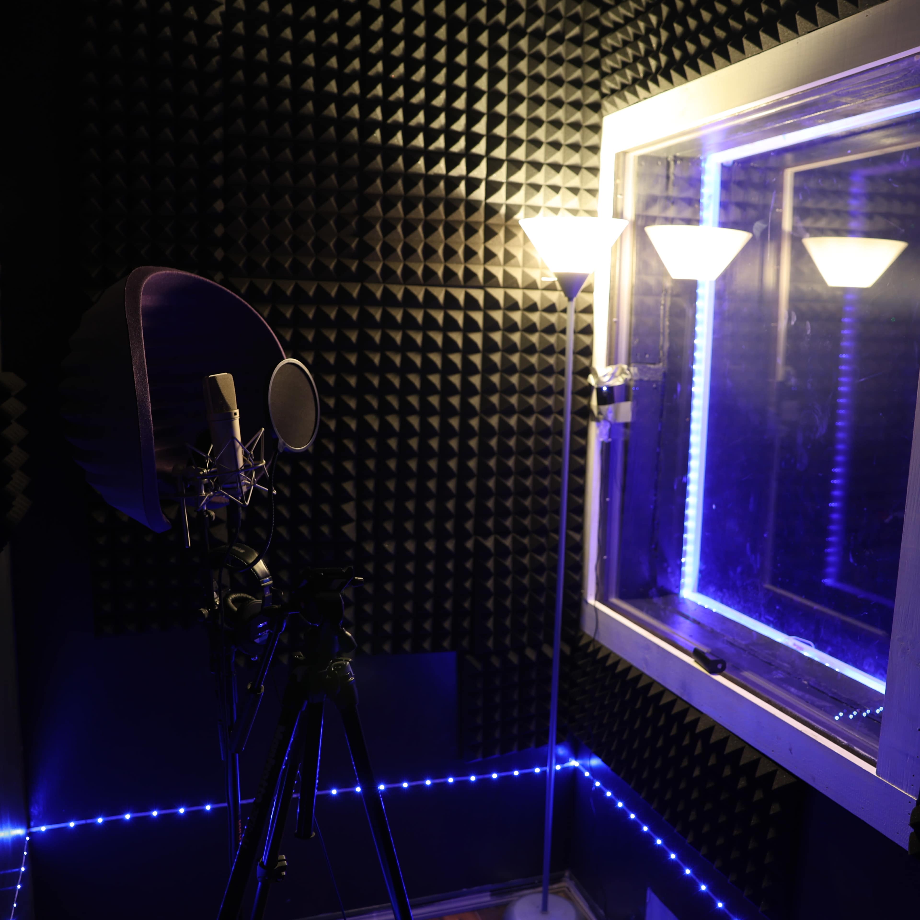 The image shows a soundproof recording booth featuring a microphone on a tripod and ambient lighting.
