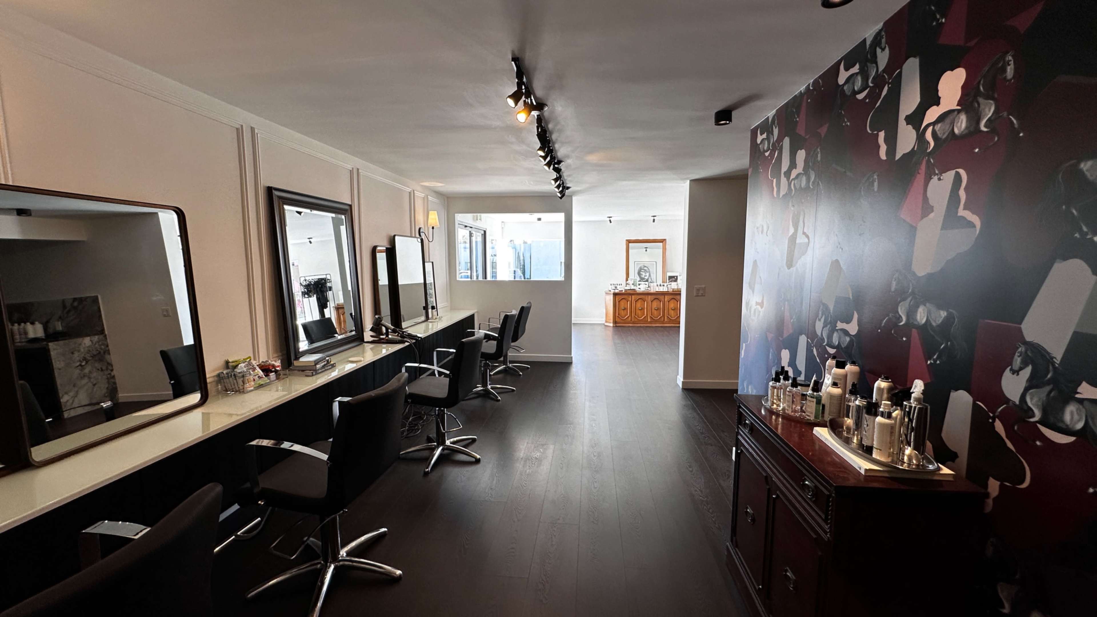 A modern hair salon featuring black styling chairs, large mirrors, and a wall adorned with abstract artwork.