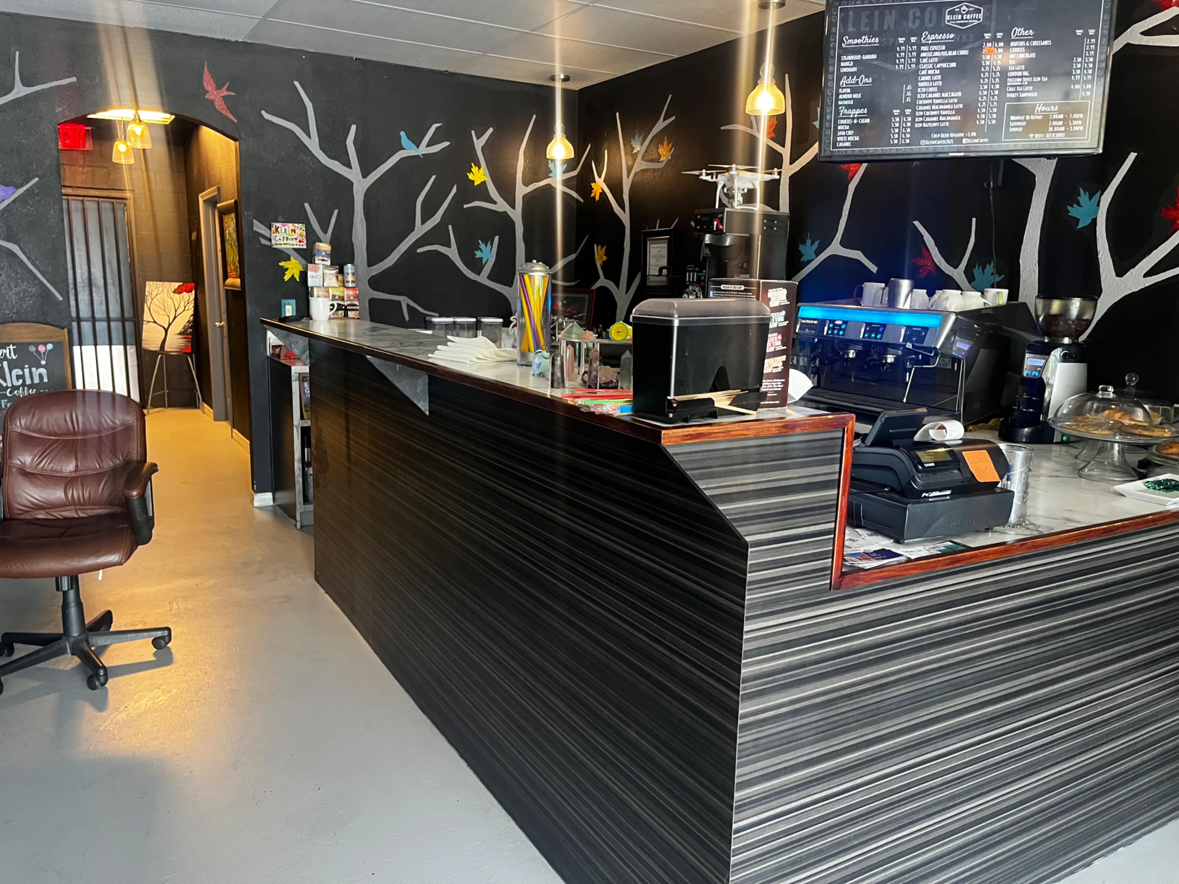 A coffee shop interior with a service counter adorned with colorful bird designs on the black walls.