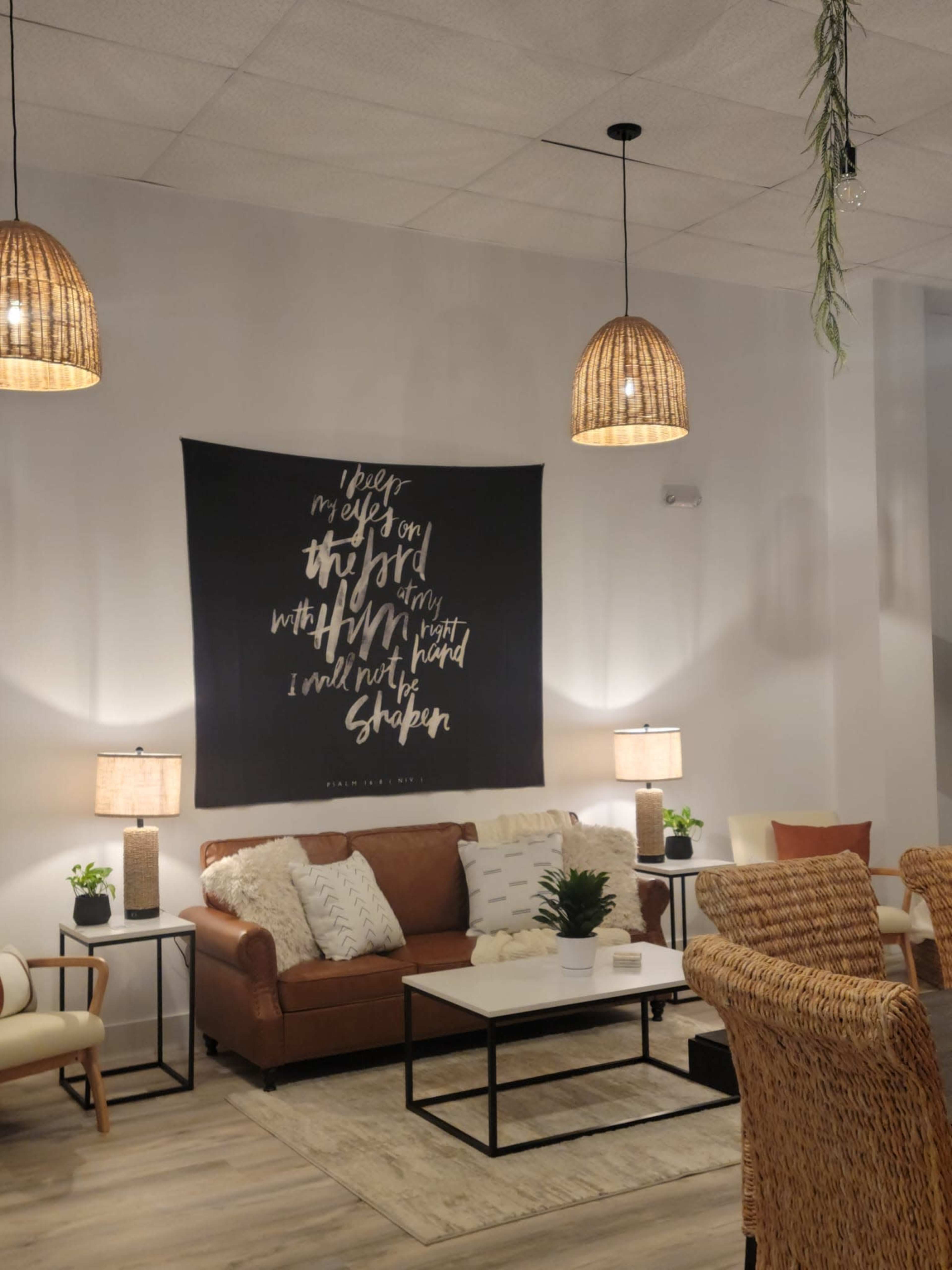 A cozy living room features a brown leather sofa, a coffee table, decorative plants, and wall art, all illuminated by pendant lights.