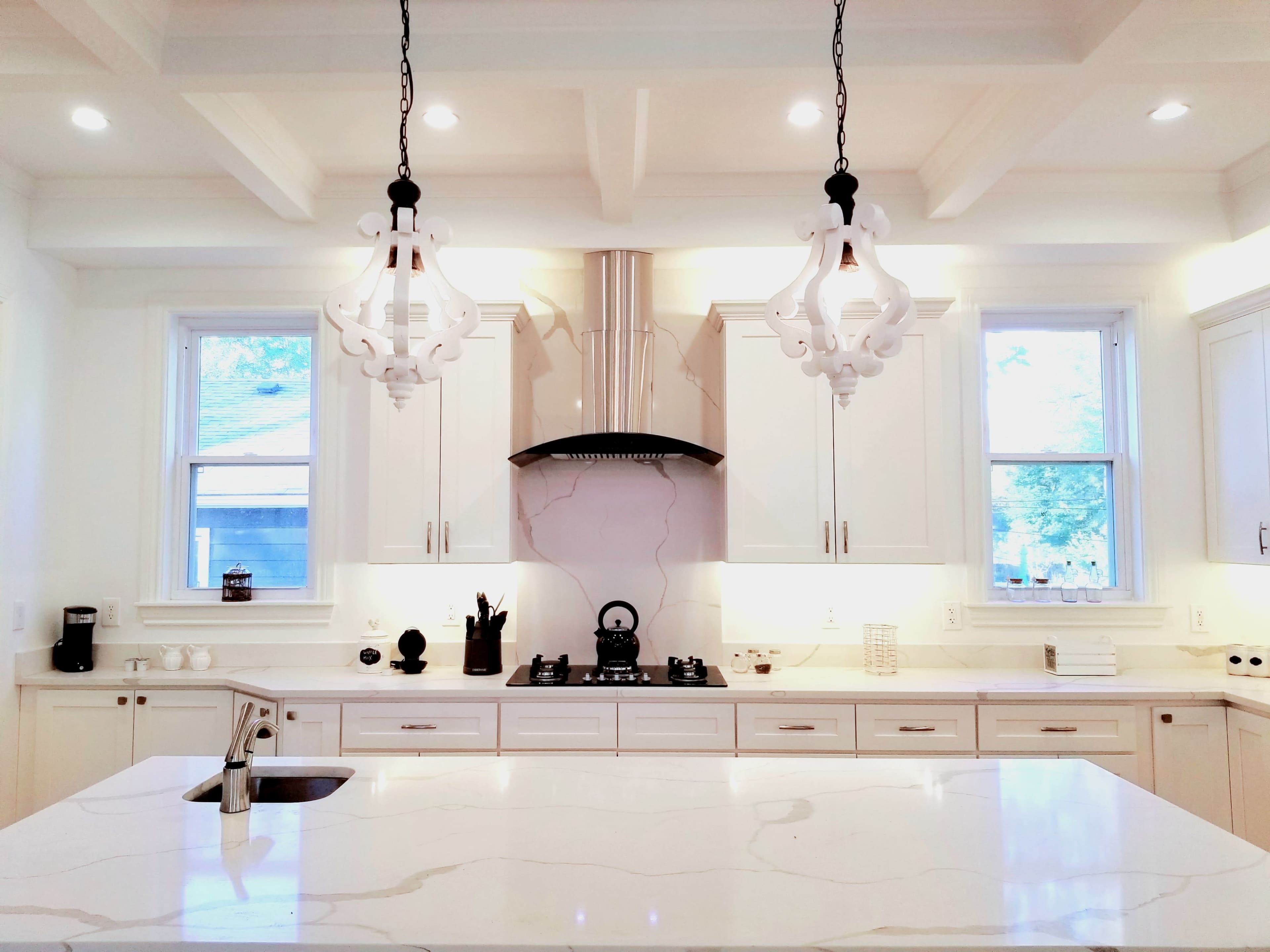 A modern kitchen features white cabinetry, a large marble island, and two pendant lights hanging above.
