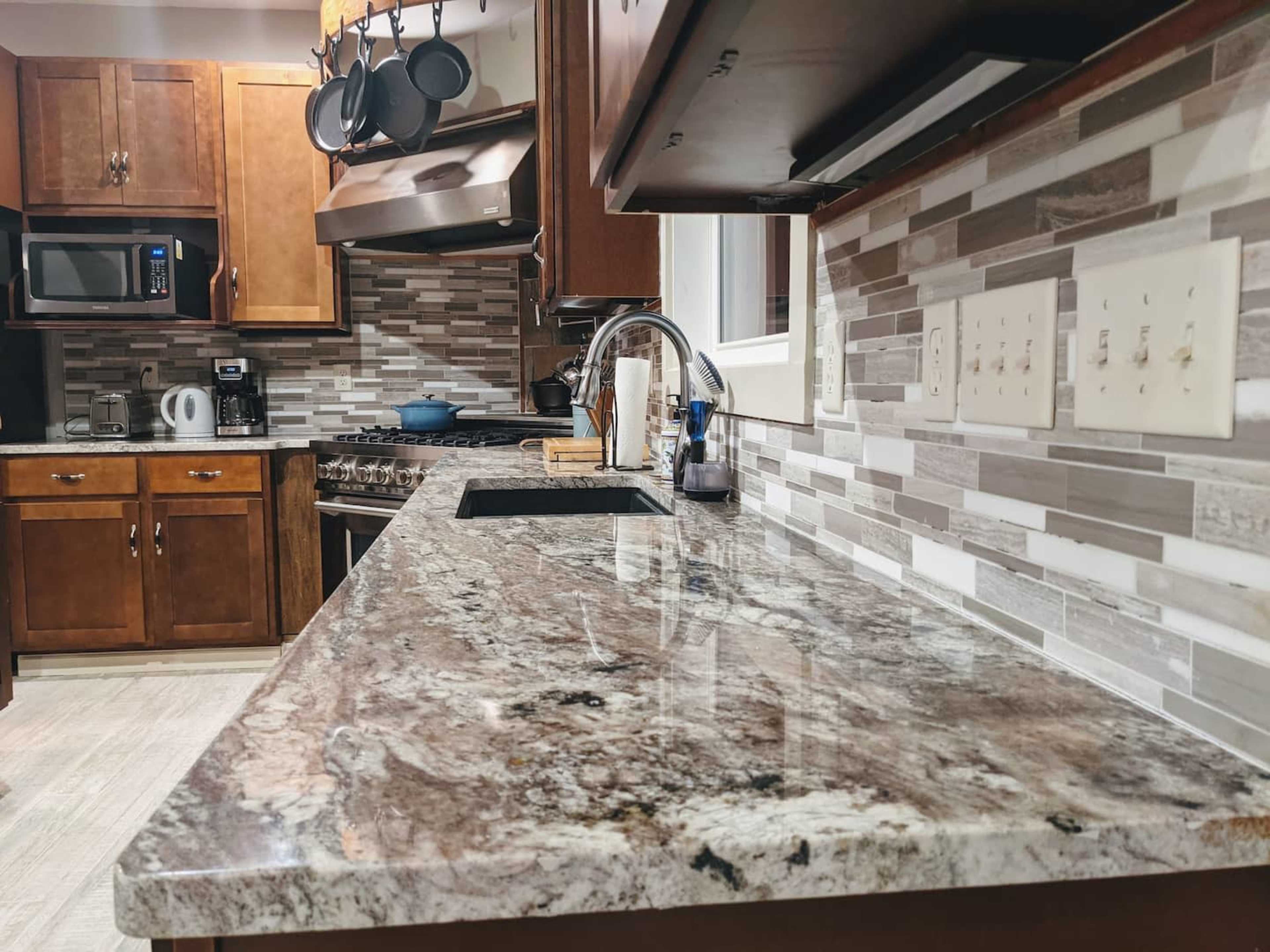 A modern kitchen with wooden cabinets, a granite countertop, and a backsplash made of light-colored tiles.