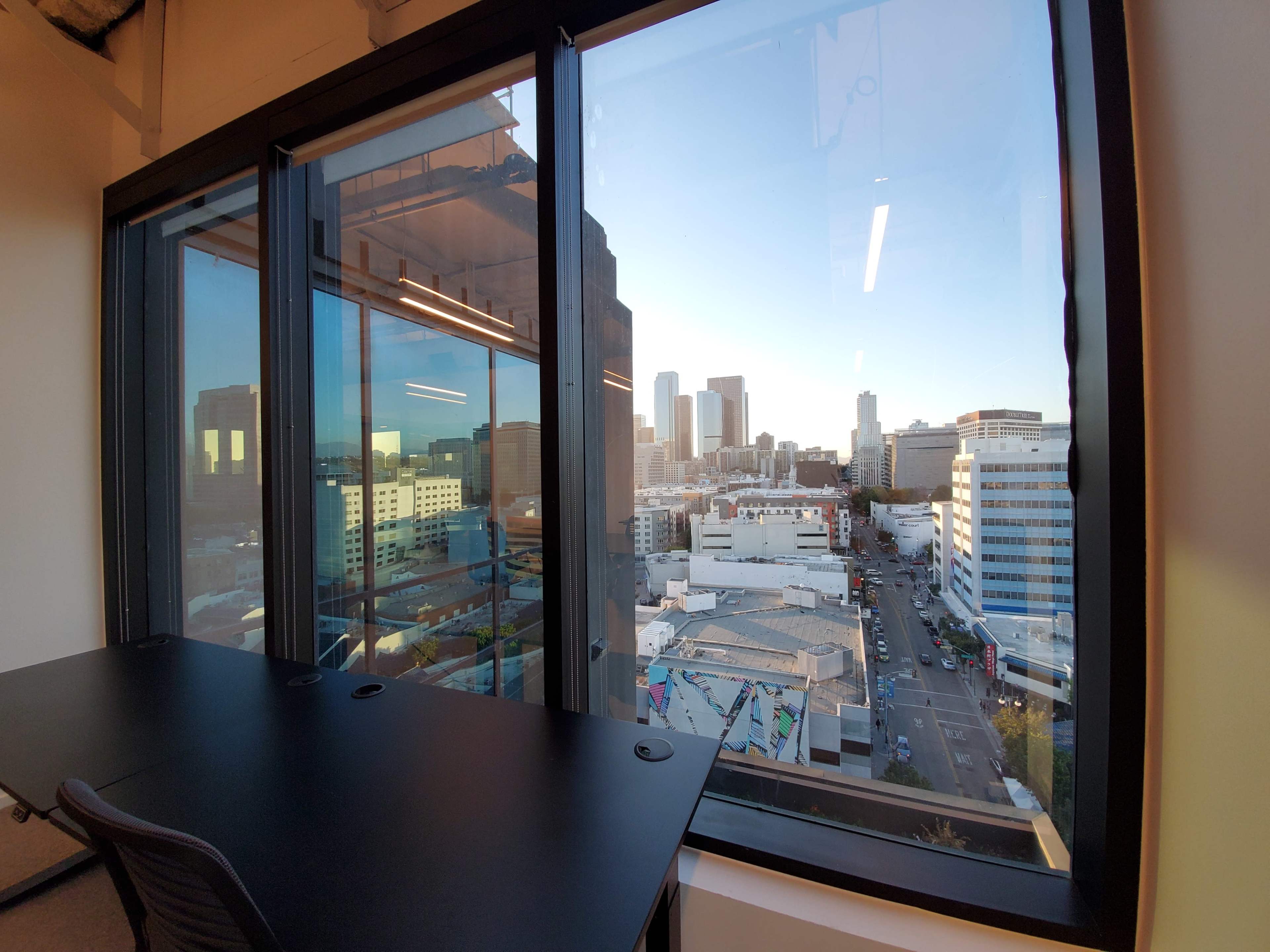 A modern office with large windows overlooking a city skyline at sunset.