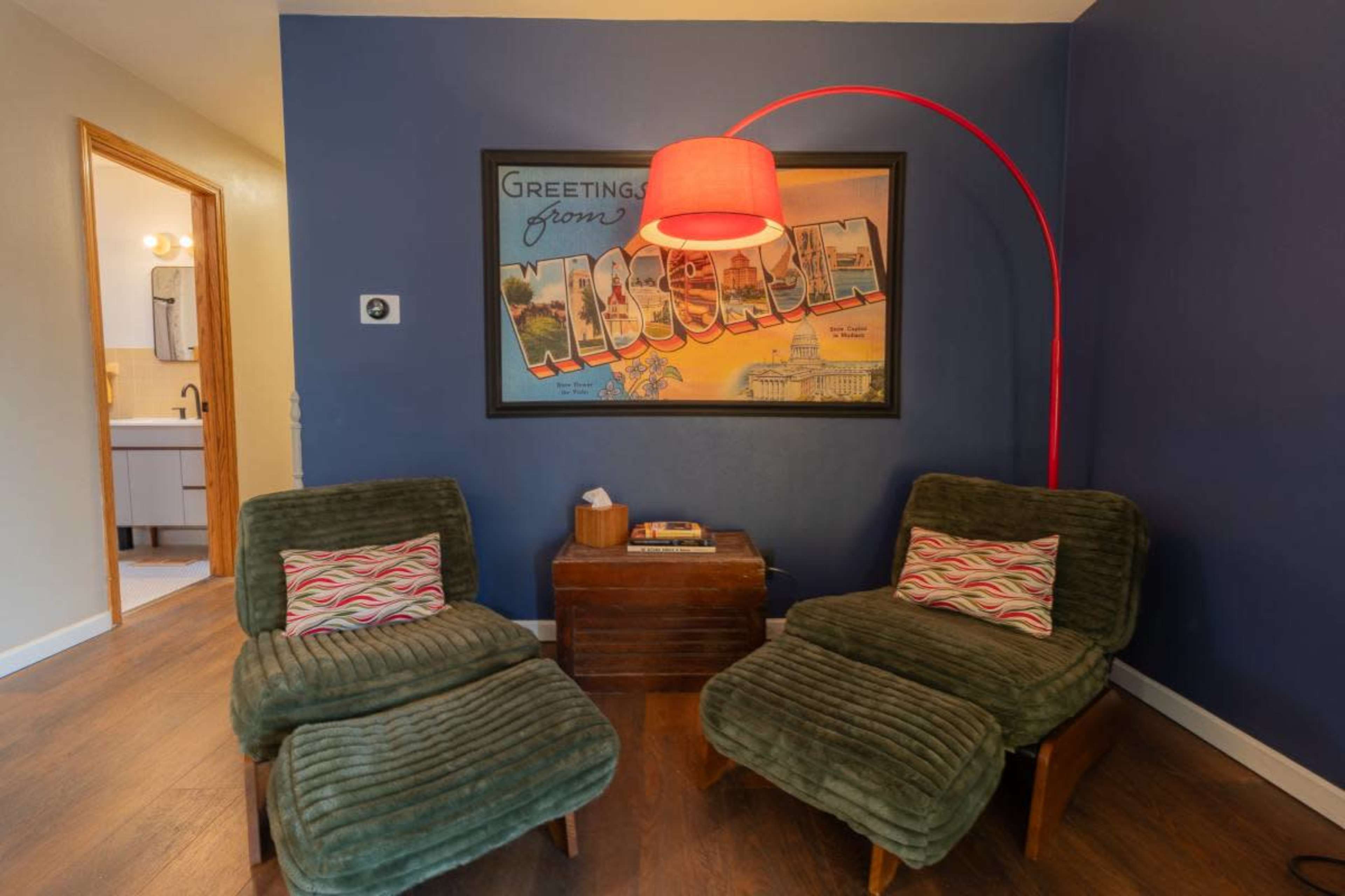 The image features a cozy corner with two green chairs, a red arc lamp, and a vintage postcard-style wall art depicting a scene from Moscow.