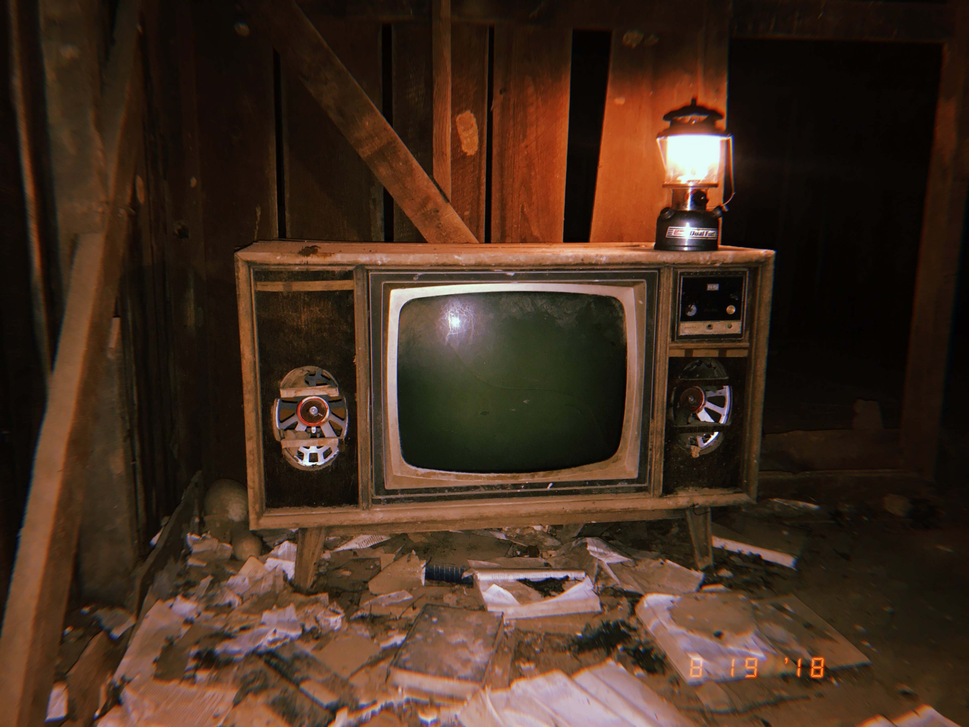 An old television set with visible speakers sits among debris in a dimly lit, abandoned room.