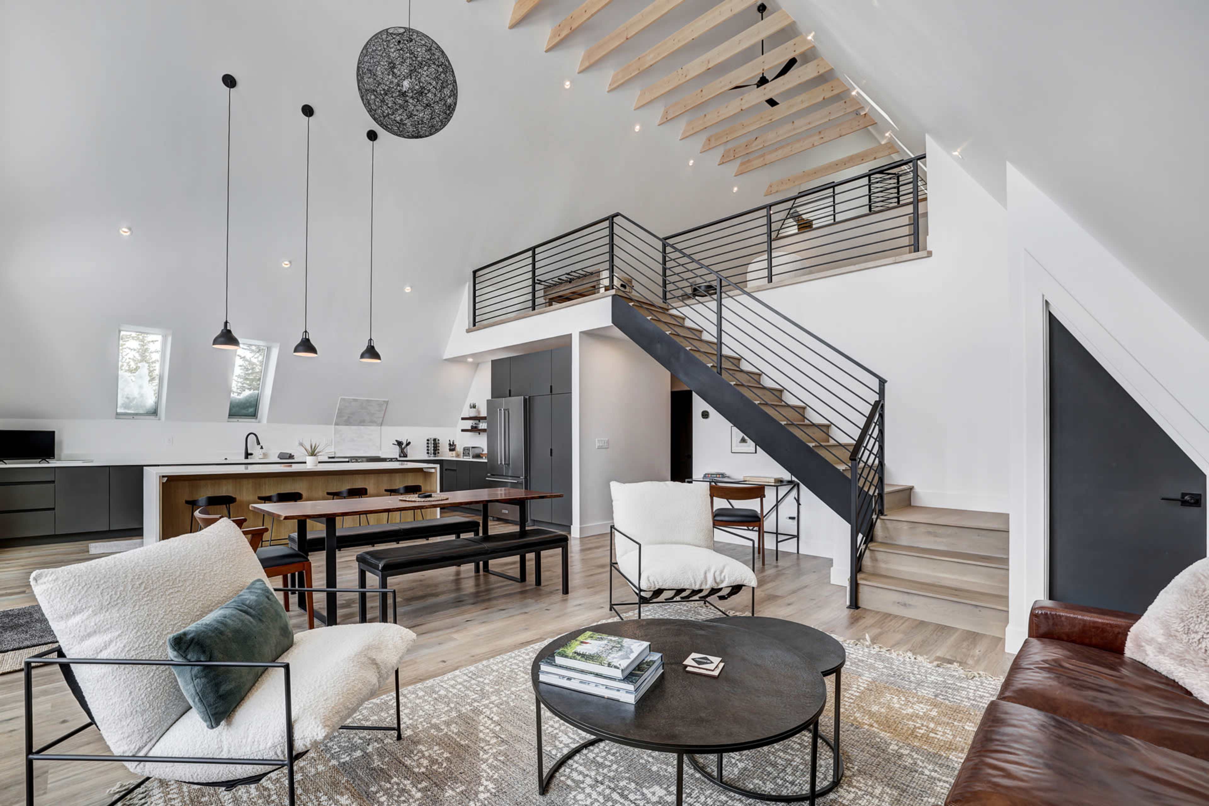 A modern, open-concept living space with a kitchen, dining area, and a staircase leading to a loft.
