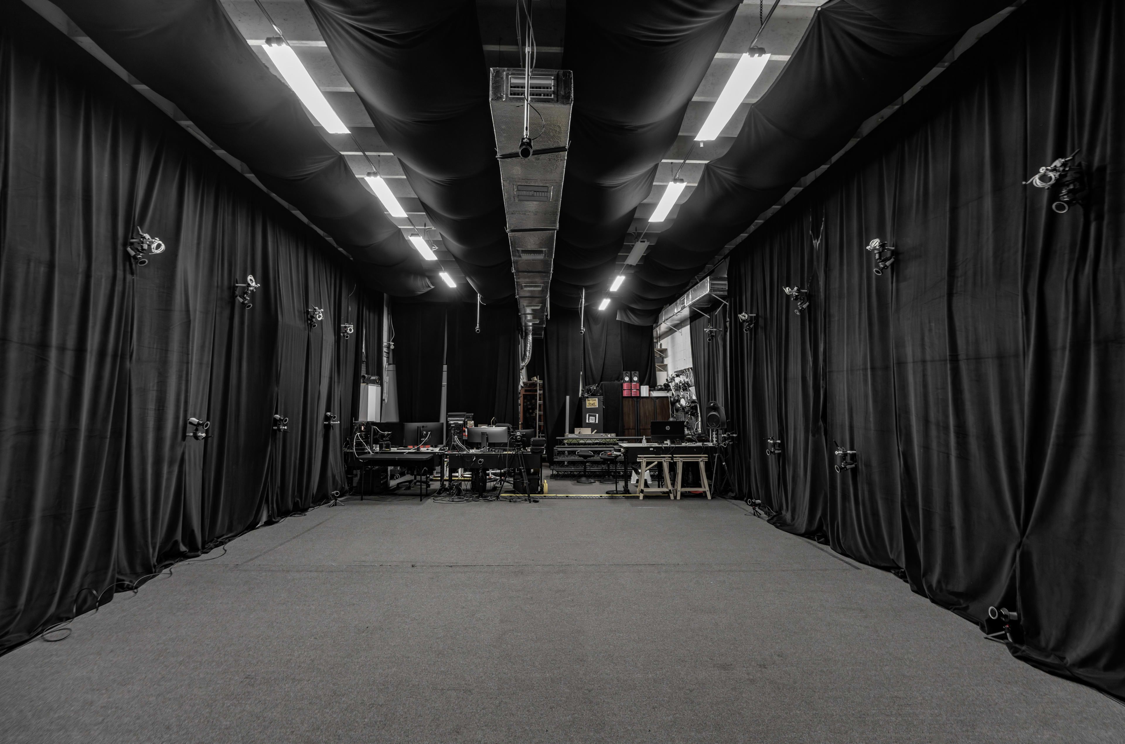 The image shows an empty studio space with black curtains lining the walls and computer equipment positioned along one side.