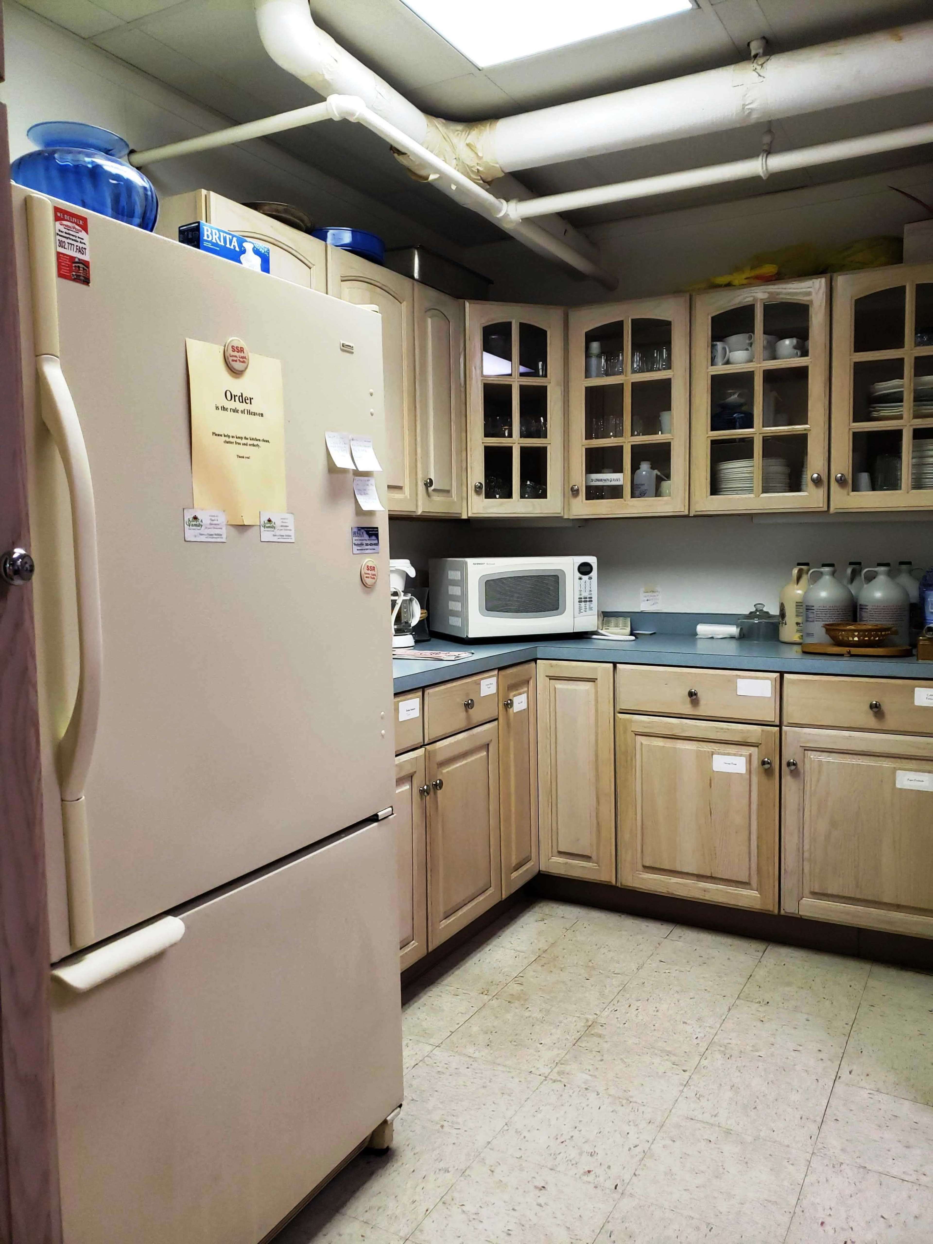 A small kitchen area with a refrigerator, microwave, and cabinetry containing dishes and utensils.