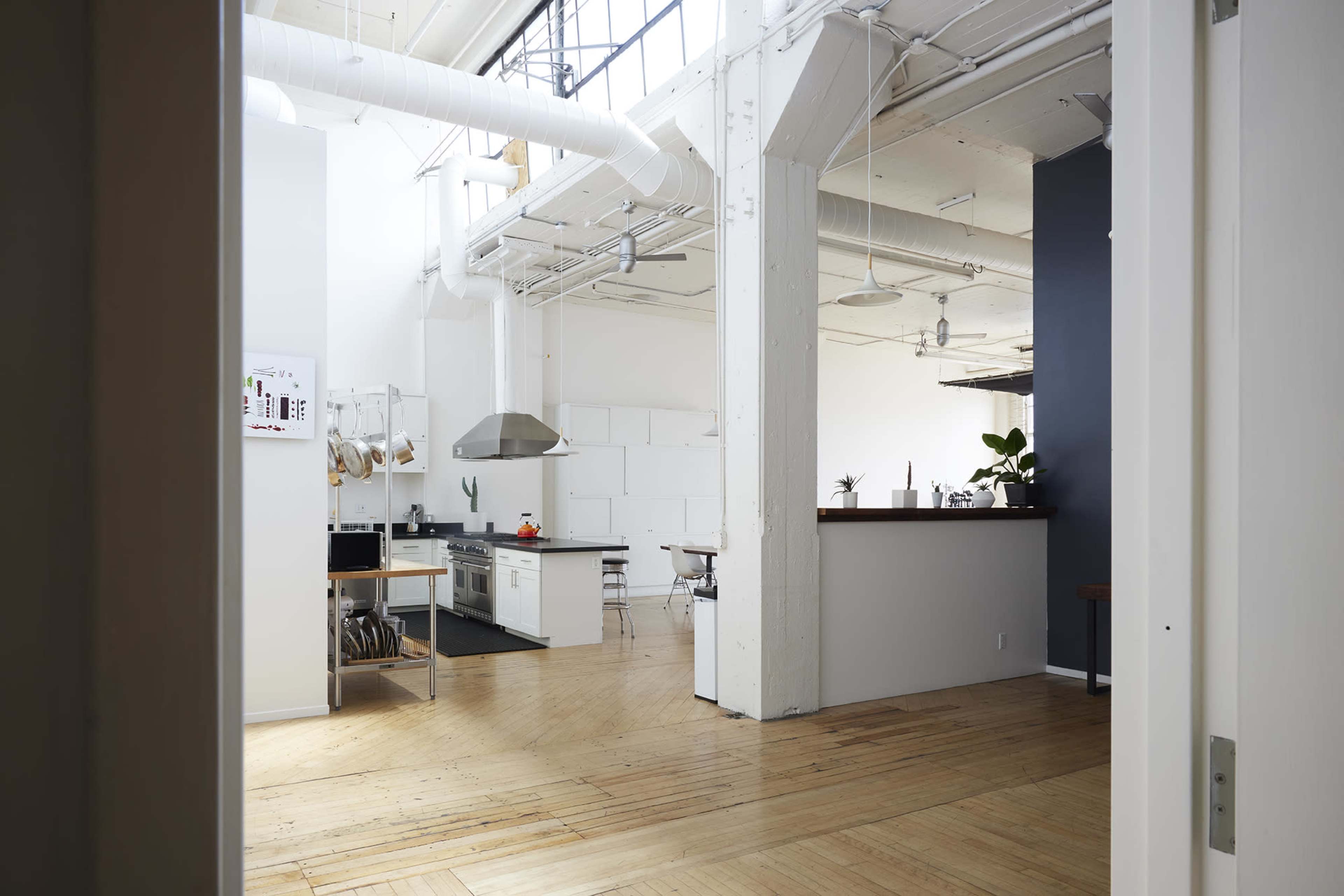 A spacious, modern kitchen area with an open layout, featuring a large island, bar stools, and a sleek design, viewed from a doorway.