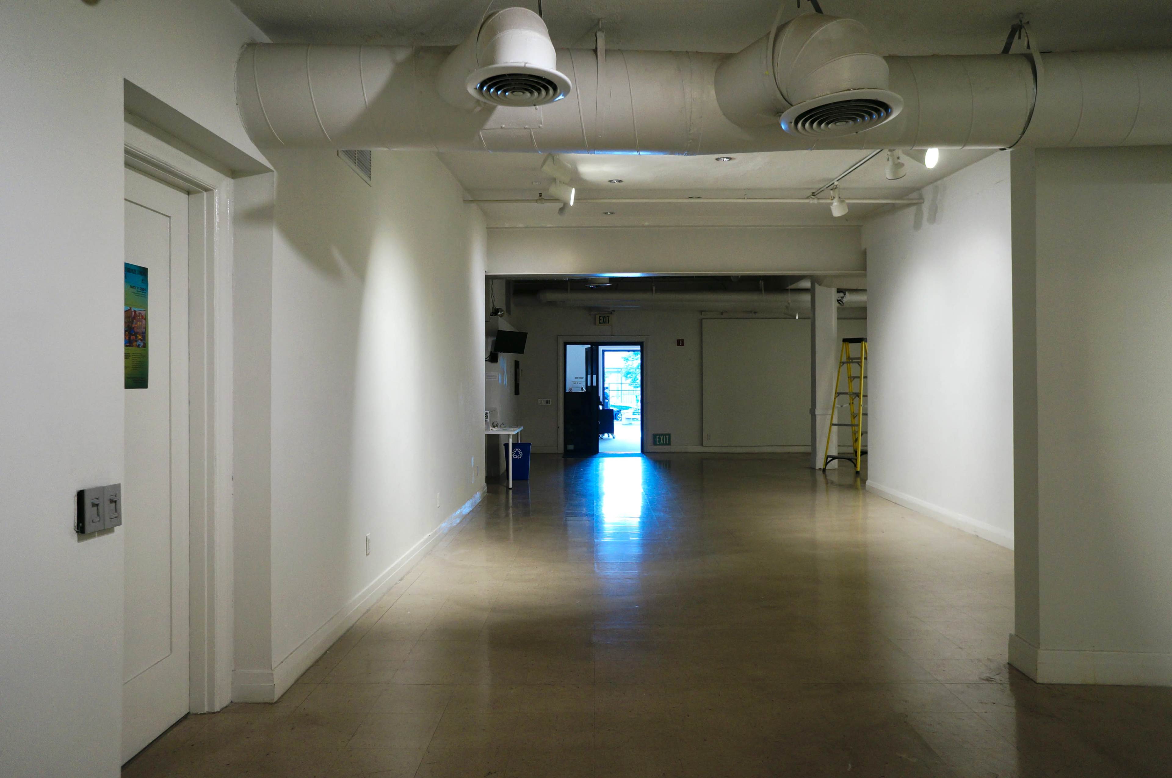 A long, empty hallway with a door at the end and overhead ductwork.