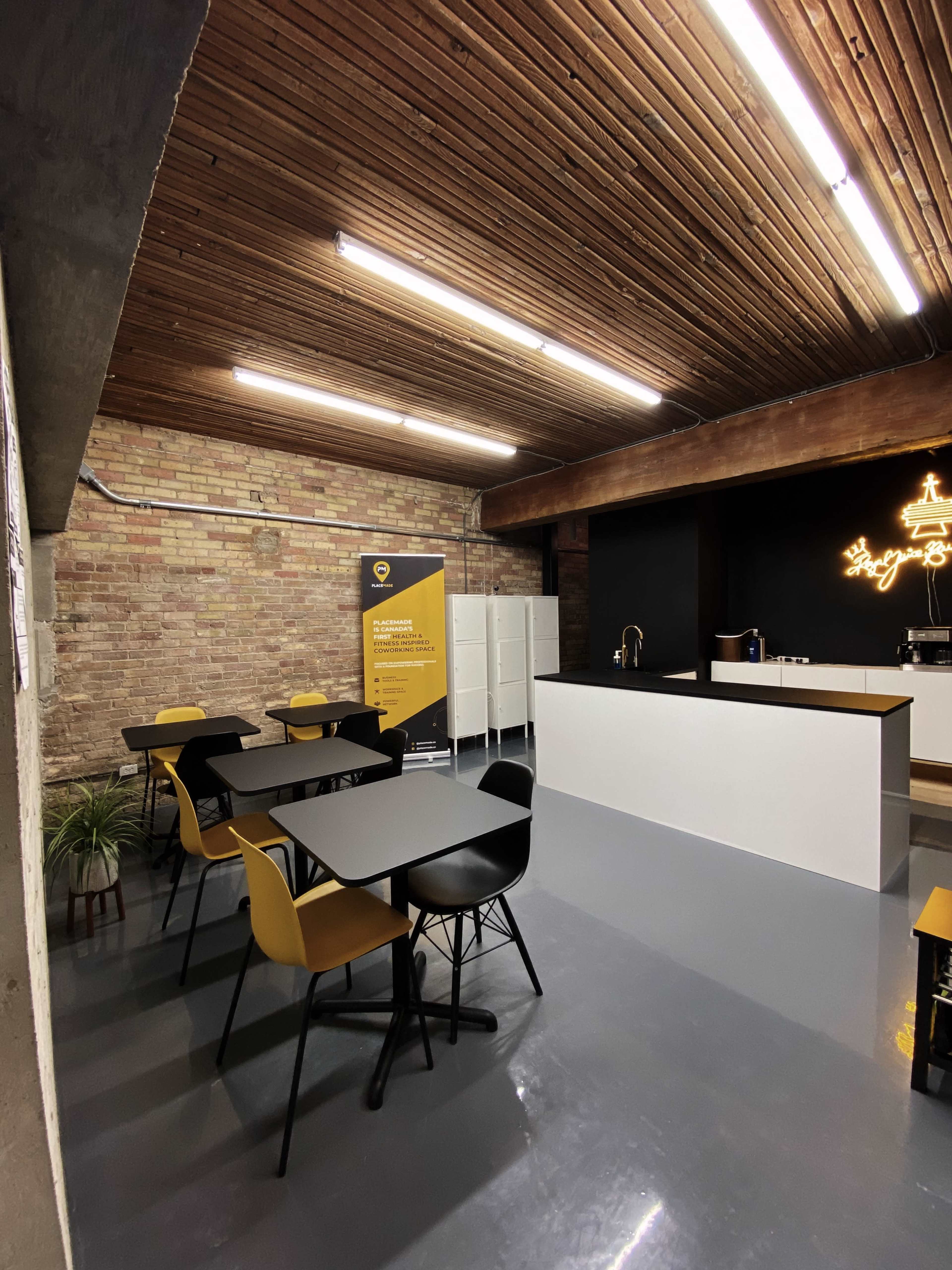 A modern, spacious break area features wooden beams, a sleek kitchen counter, and several tables with black and yellow chairs.