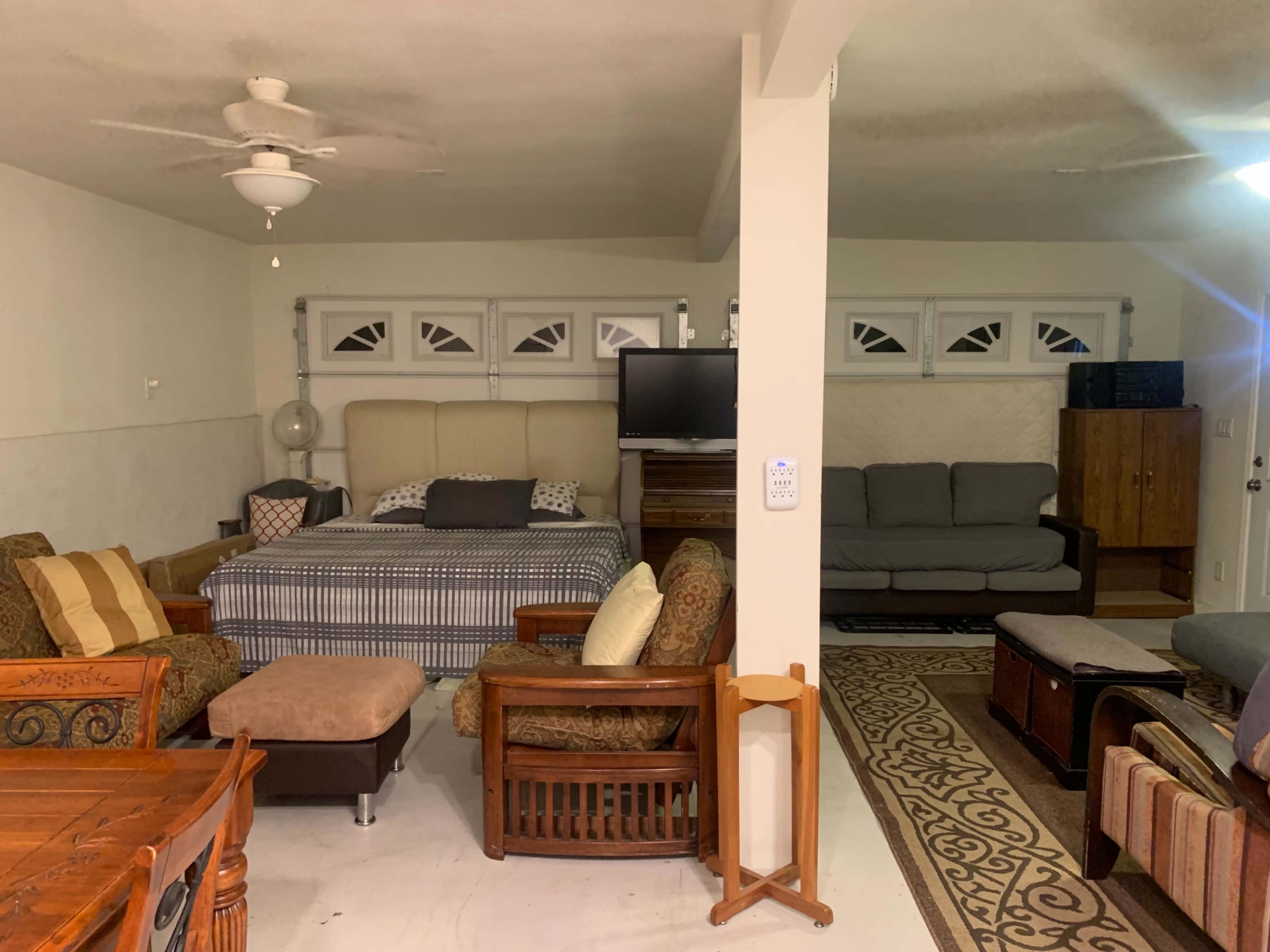 A spacious living area furnished with various seating options, including a sofa, armchairs, and a bed, alongside a dining table and a television setup.