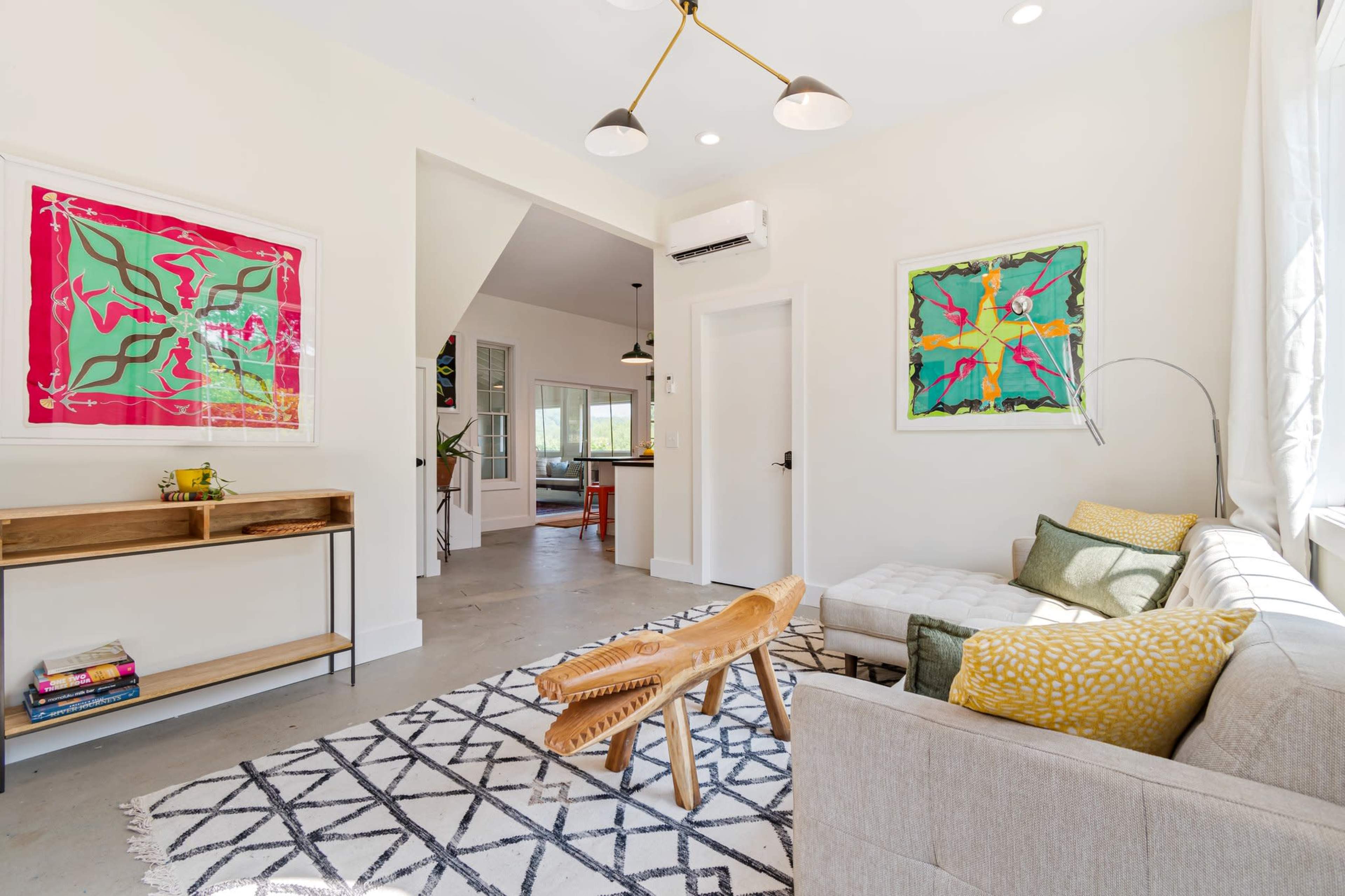A modern living room with a light-colored sofa, a wooden bench, and colorful wall art, featuring a patterned rug on the floor.